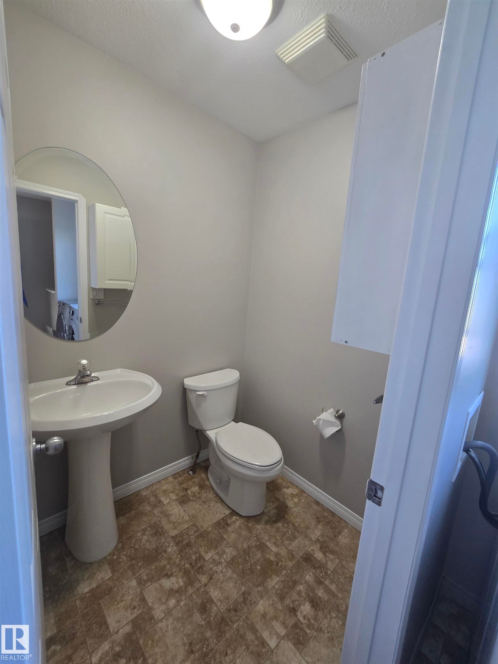 Compact powder room featuring a pedestal sink, white toilet, patterned vinyl flooring, and a round wall mirror - 4120 47 Street, Drayton Valley, AB - Indoor Photo Showing Bathroom