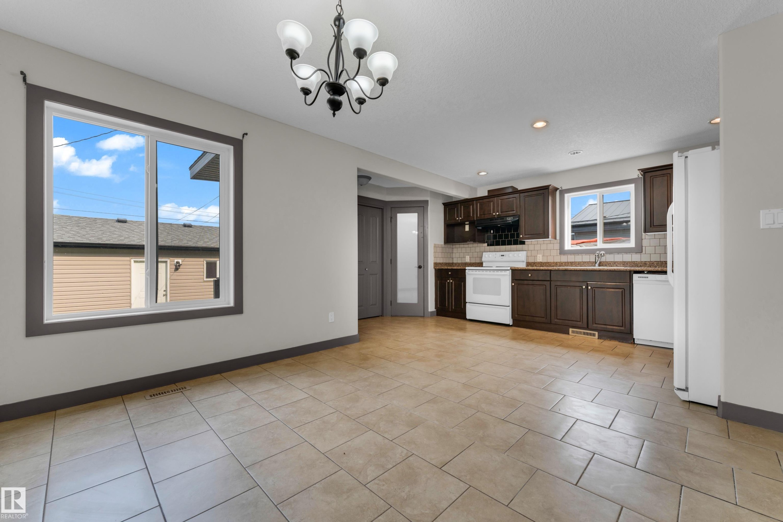 Open-concept space featuring ceramic tile flooring, a kitchen with dark wood-finish cabinetry, and white appliances - 11817 37 Street Nw, Edmonton, AB - Indoor Photo Showing Kitchen