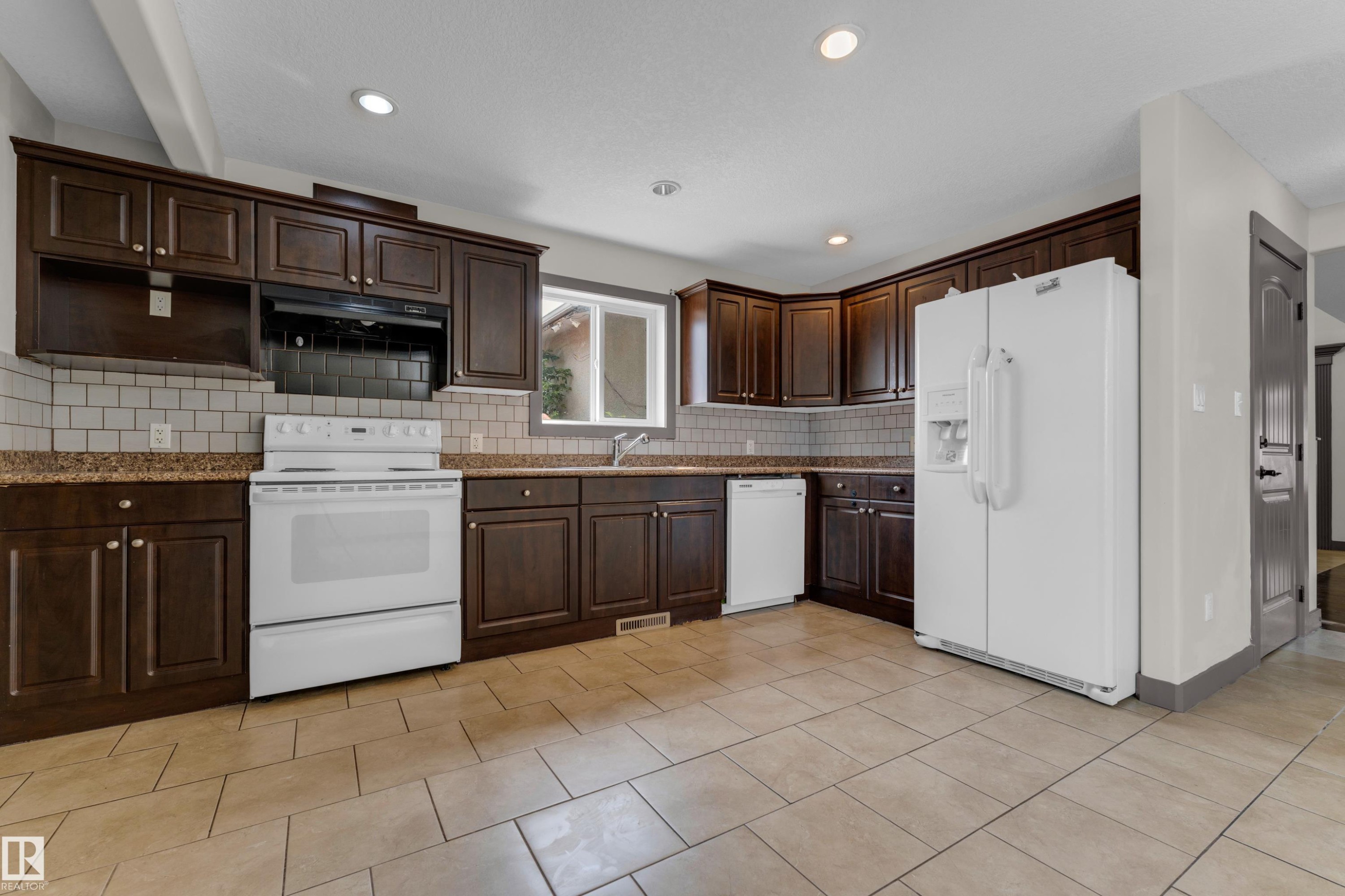 Kitchen featuring dark wood cabinetry, light-toned tile flooring, subway tile backsplash, and white appliances - 11817 37 Street Nw, Edmonton, AB - Indoor Photo Showing Kitchen
