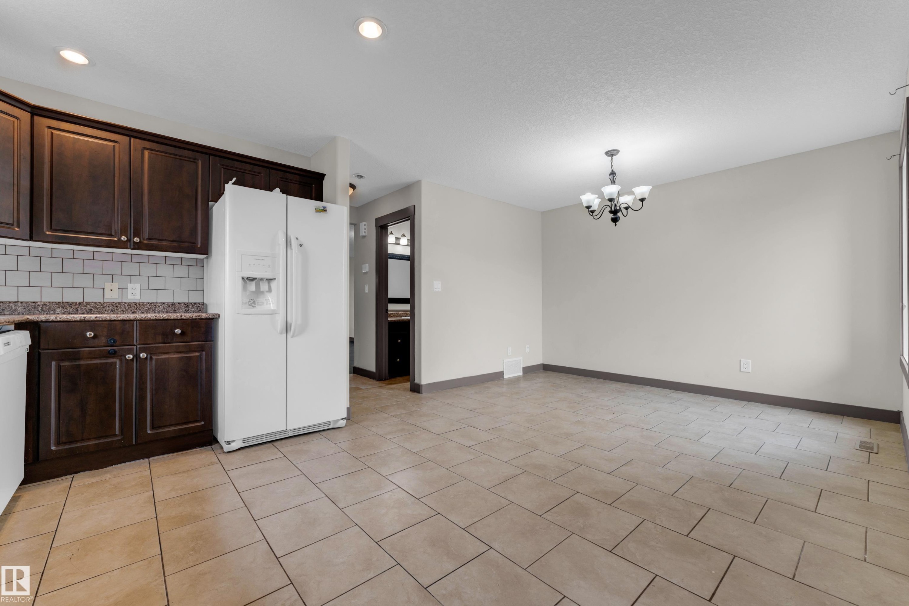 Kitchen and dining area featuring dark wood cabinetry, a subway tile backsplash, and light-toned tile flooring - 11817 37 Street Nw, Edmonton, AB - Indoor Photo Showing Kitchen
