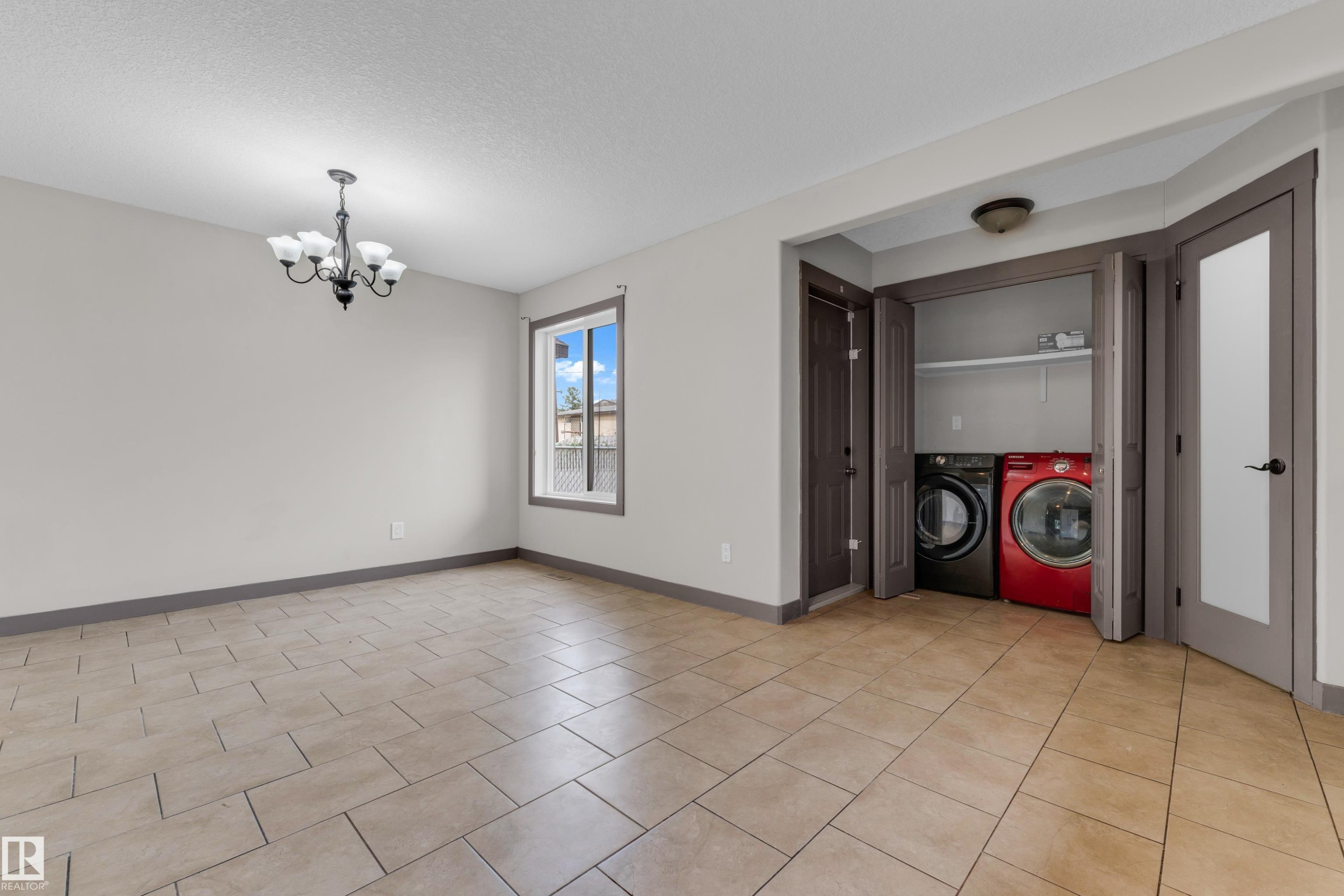 Spacious room featuring tile flooring, a window with exterior views, and a multi-light chandelier - 11817 37 Street Nw, Edmonton, AB - Indoor