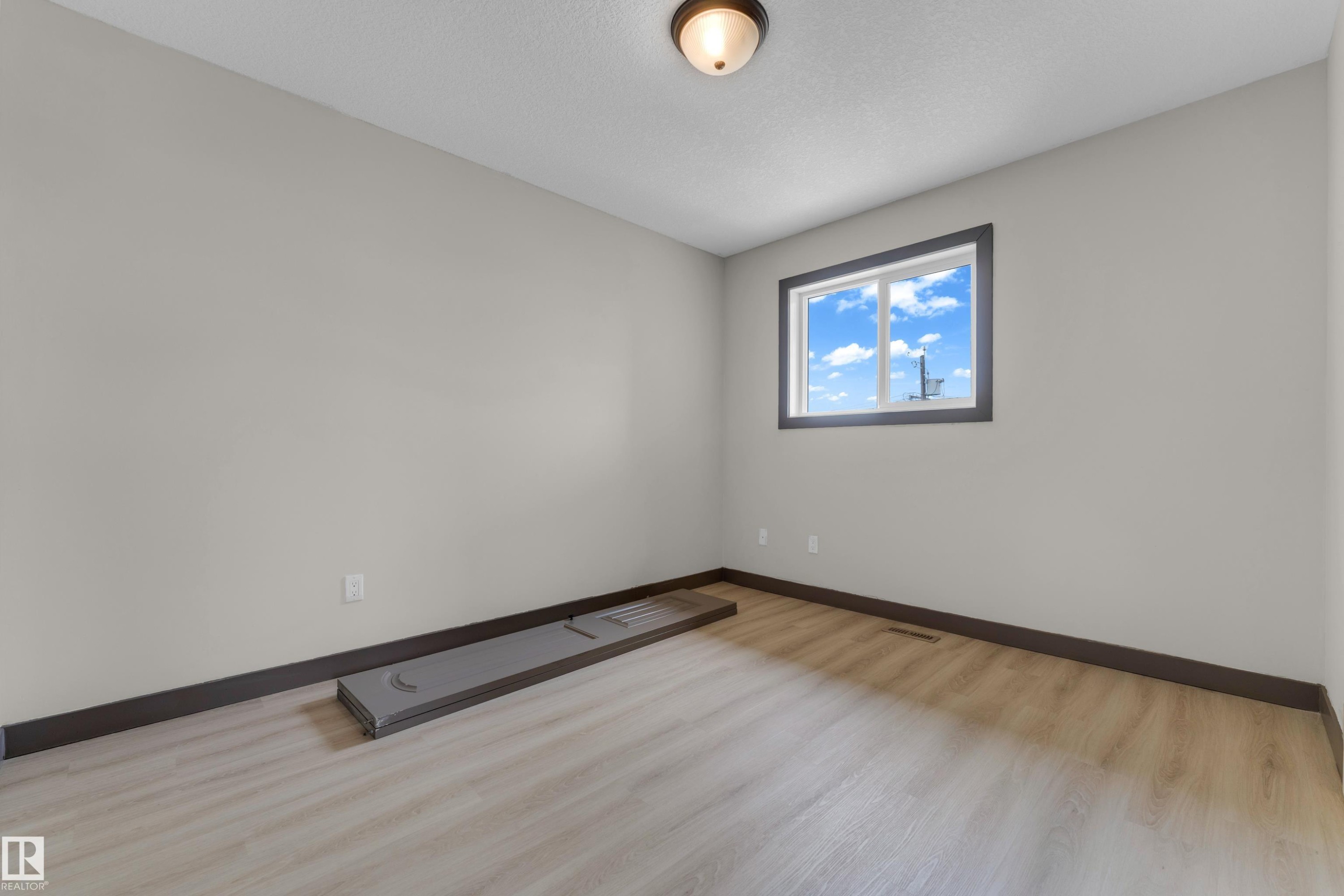 Neutral wall finishes with contrasting dark trim, wood-finish flooring, and a flush mount ceiling light fixture - 11817 37 Street Nw, Edmonton, AB - Indoor Photo Showing Other Room
