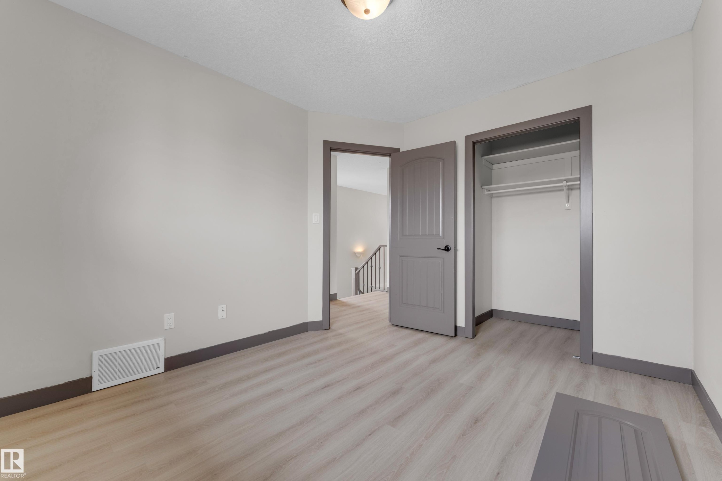 Spacious room featuring light wood-finish flooring, neutral gray walls, a built-in closet with shelving and hanging rod, and a coordinating gray paneled door - 11817 37 Street Nw, Edmonton, AB - Indoor Photo Showing Other Room