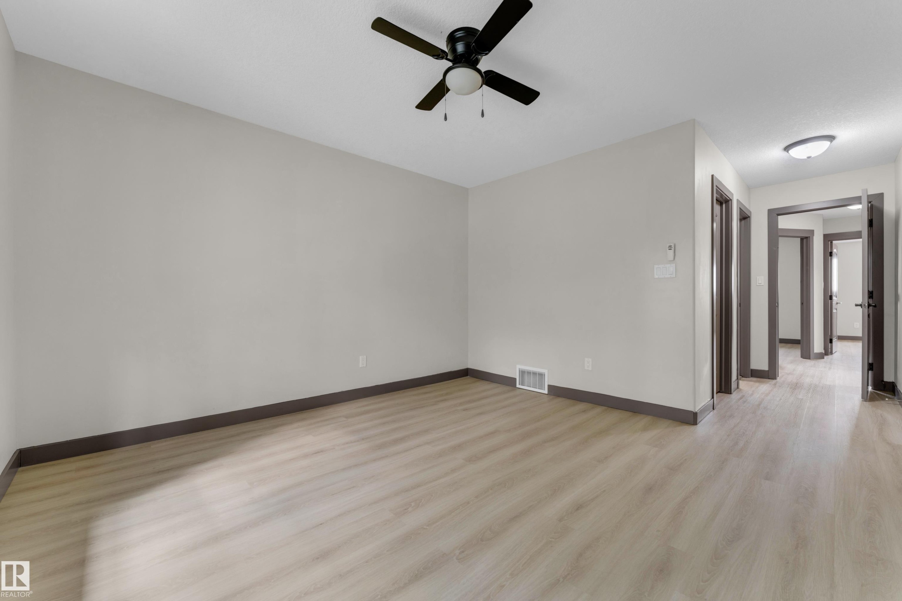 Spacious room with light wood-finish flooring, light gray wall paint, and contrasting dark baseboards - 11817 37 Street Nw, Edmonton, AB - Indoor Photo Showing Other Room