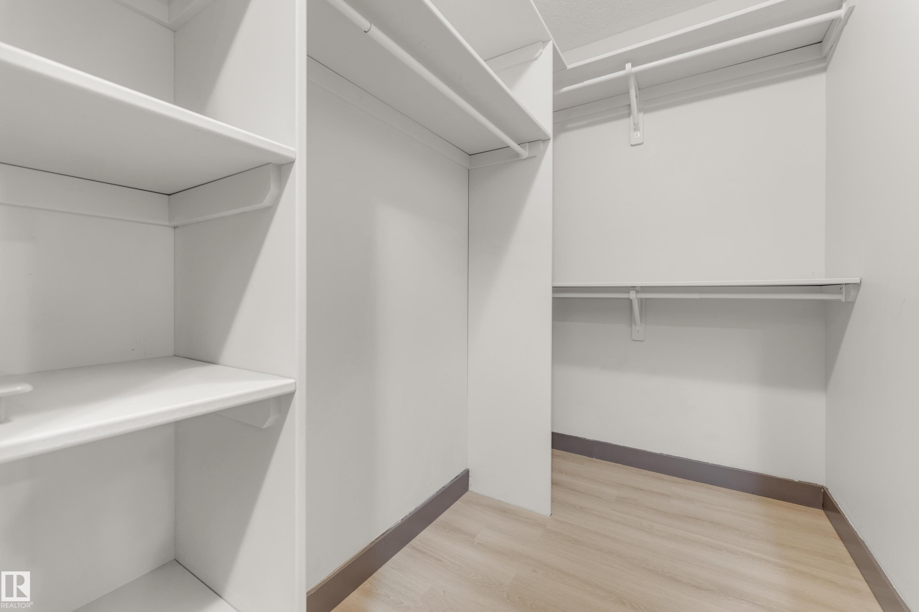Walk-in closet featuring white walls, wood-finish flooring, and ample storage with multiple shelving units and clothing rods - 11817 37 Street Nw, Edmonton, AB - Indoor With Storage