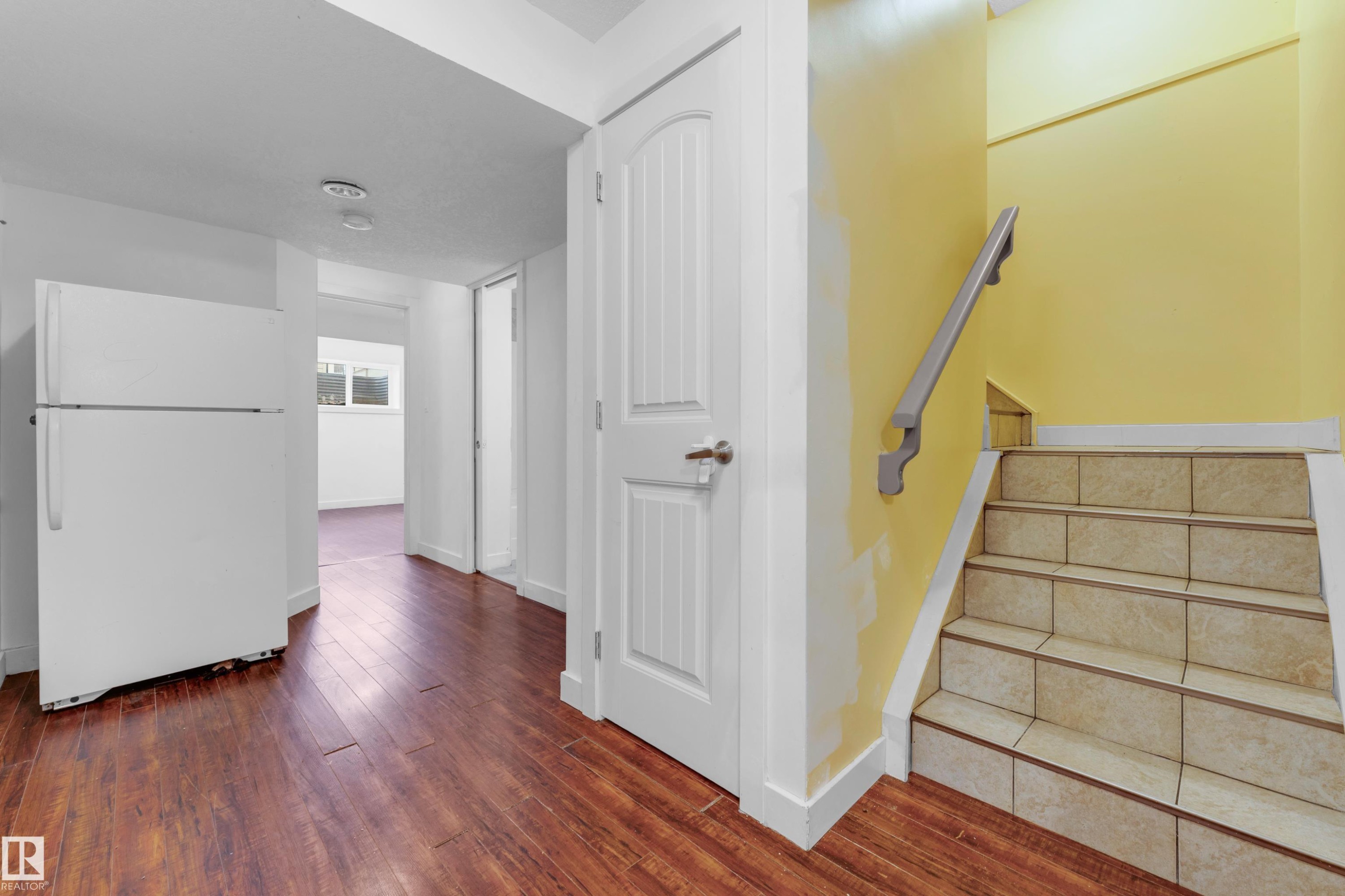 Interior space featuring rich wood-finish flooring, a white refrigerator, a paneled door, and a staircase with tile treads and a handrail - 11817 37 Street Nw, Edmonton, AB - Indoor Photo Showing Other Room