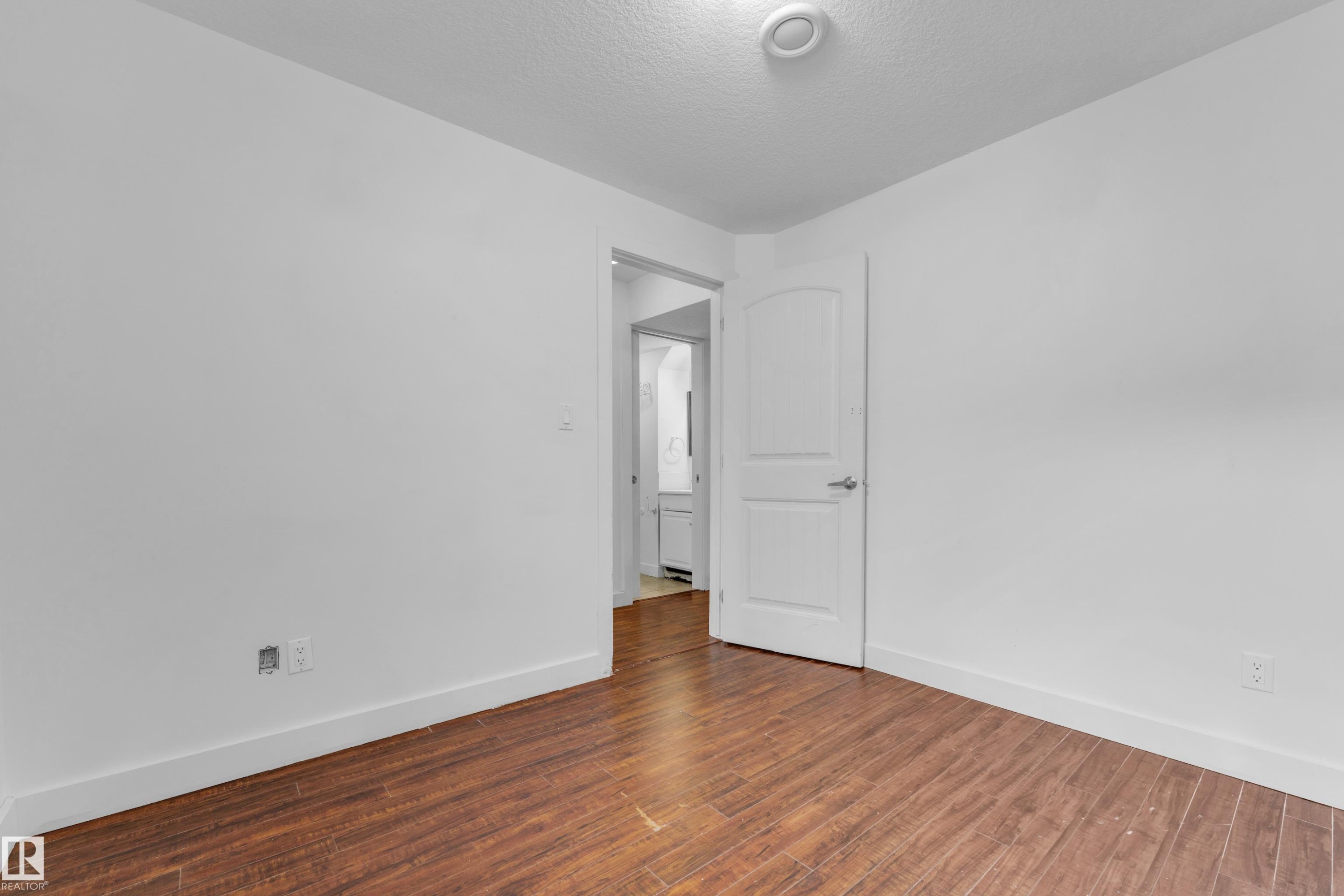 Room featuring wood-finish flooring, white baseboards, and a white interior door with a silver handle - 11817 37 Street Nw, Edmonton, AB - Indoor Photo Showing Other Room
