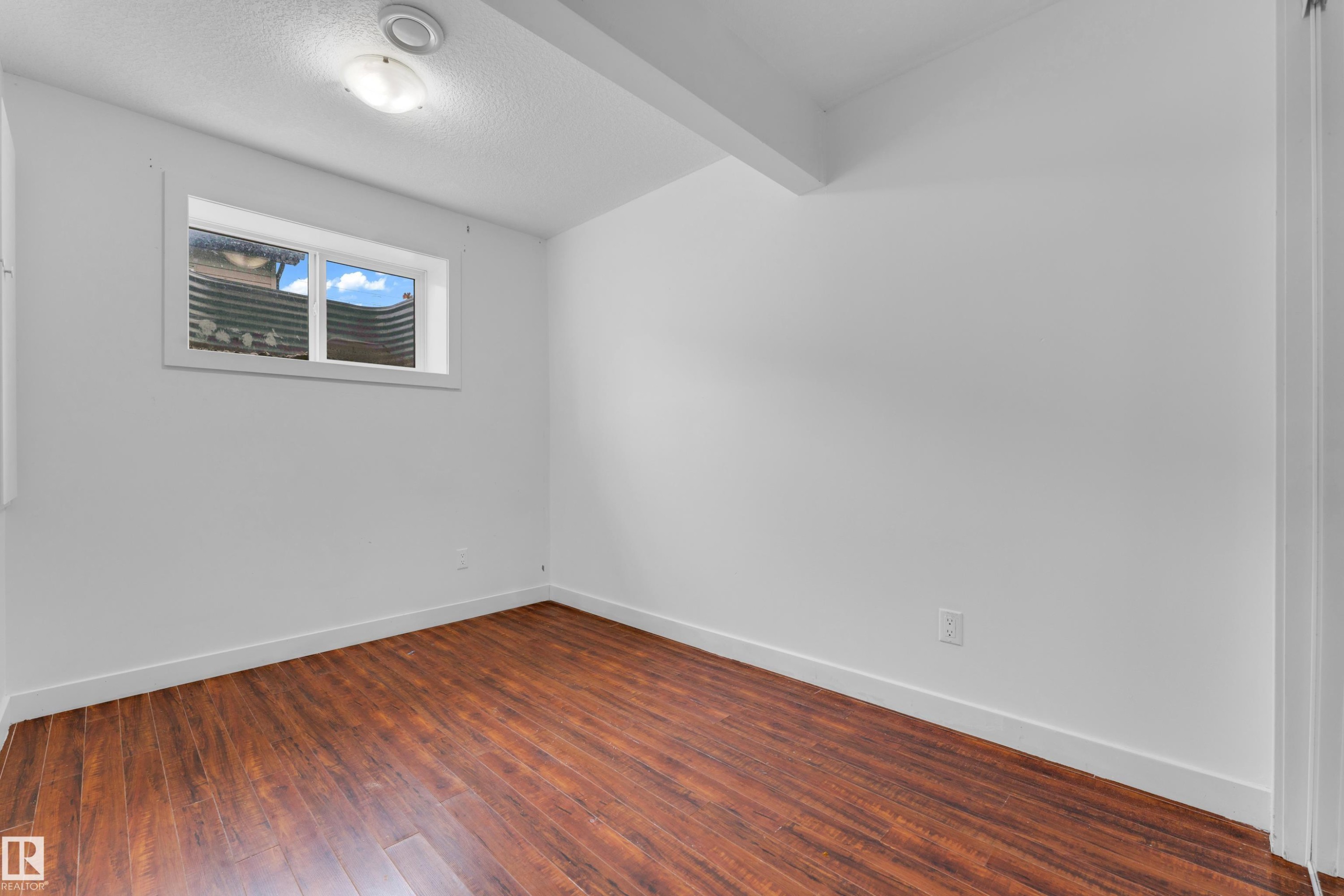 Room featuring wood-finish flooring, white walls, and a window with a white frame - 11817 37 Street Nw, Edmonton, AB - Indoor Photo Showing Other Room