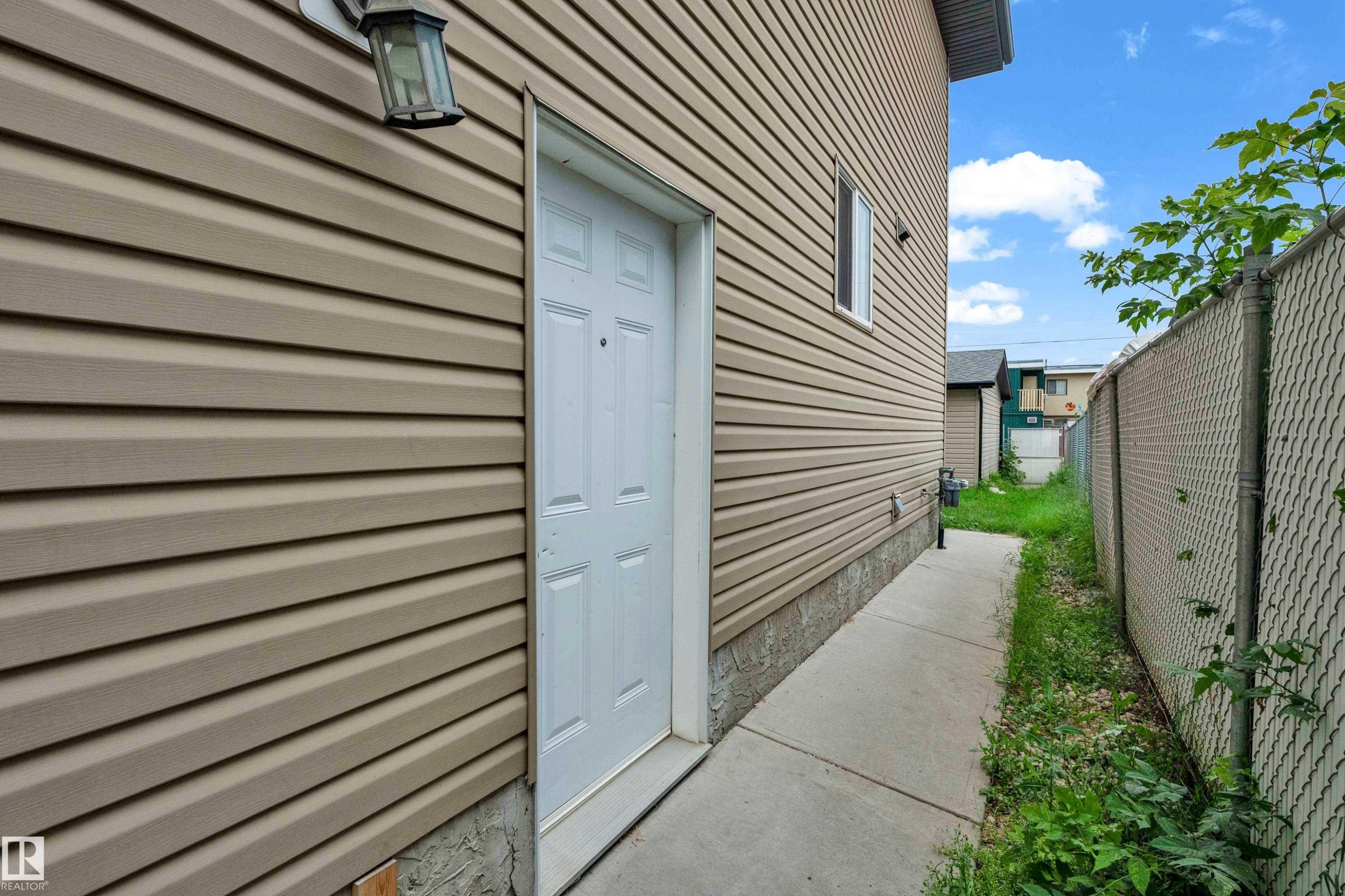 Tan horizontal vinyl siding with a white panel door and exterior light fixture - 11817 37 Street Nw, Edmonton, AB - Outdoor With Exterior