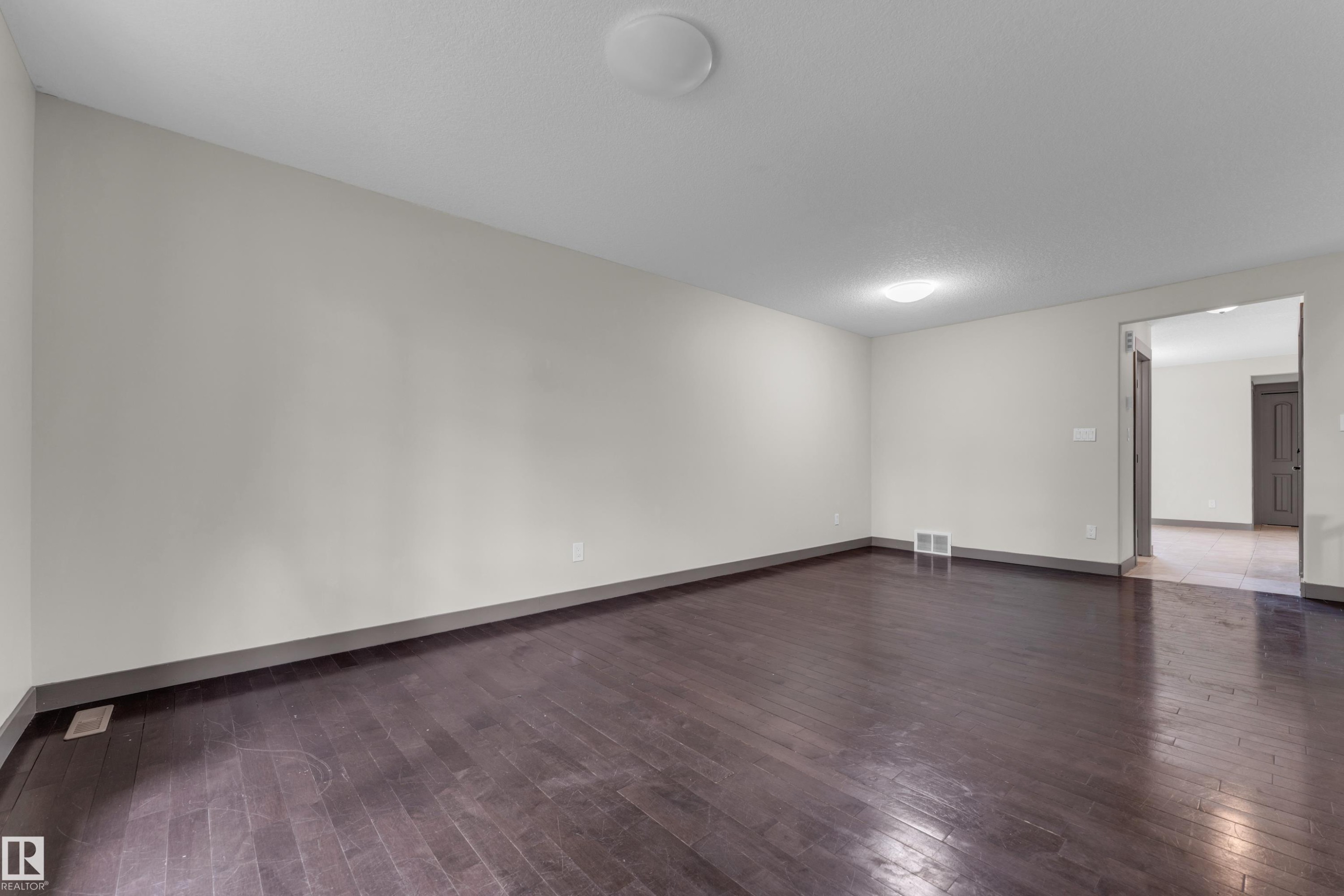 Spacious interior room featuring dark wood-finish flooring, light-toned wall paint, and a neutral baseboard trim - 11817 37 Street Nw, Edmonton, AB - Indoor Photo Showing Other Room