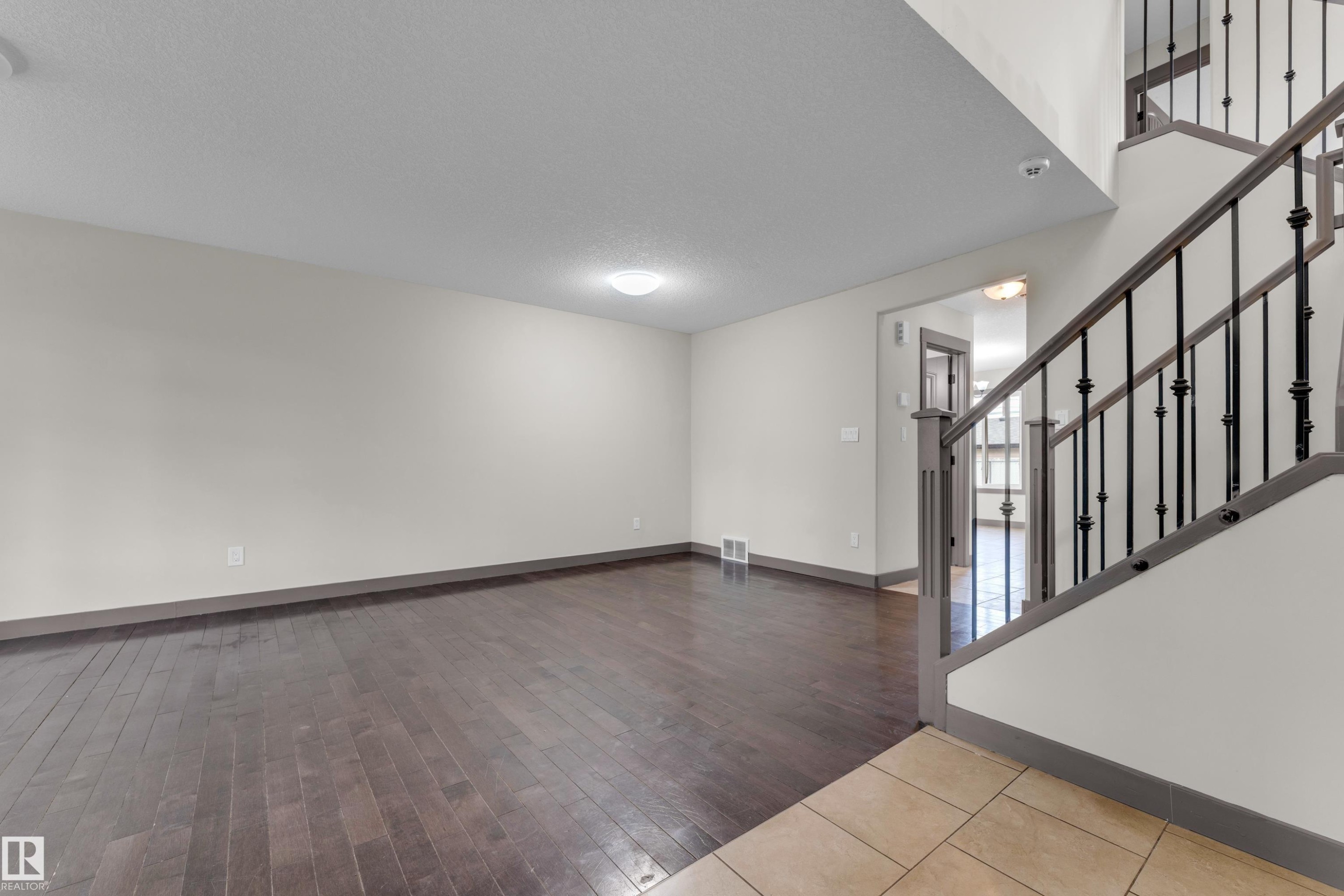 Expansive living area featuring dark wood-finish flooring, light-toned walls, and a contemporary flush-mount ceiling light - 11817 37 Street Nw, Edmonton, AB - Indoor Photo Showing Other Room