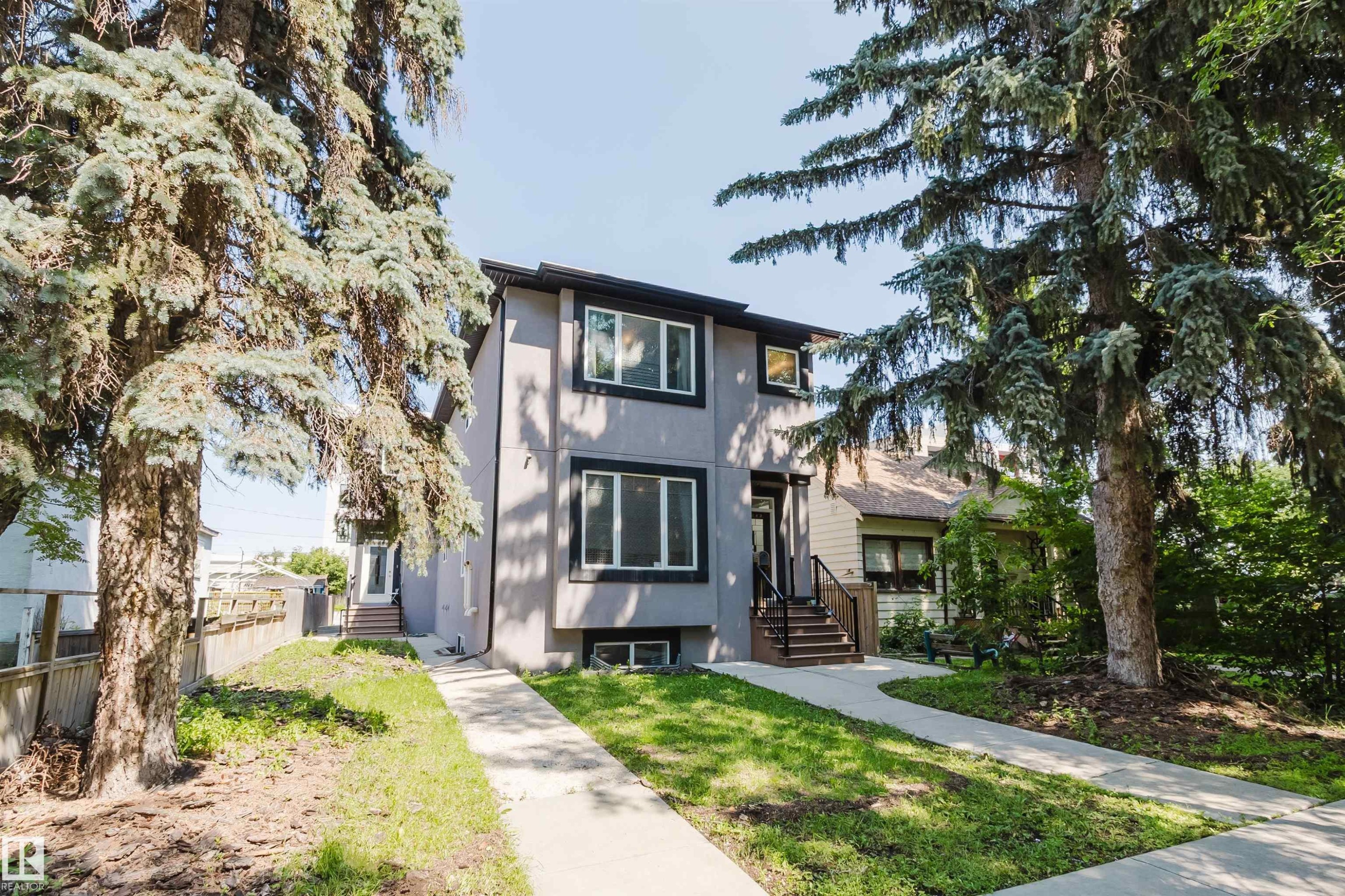 Gray stucco exterior featuring dark trim, multiple windows, and a prominent front entrance with dark railings - 10626 81 Avenue Nw, Edmonton, AB - Outdoor With Facade