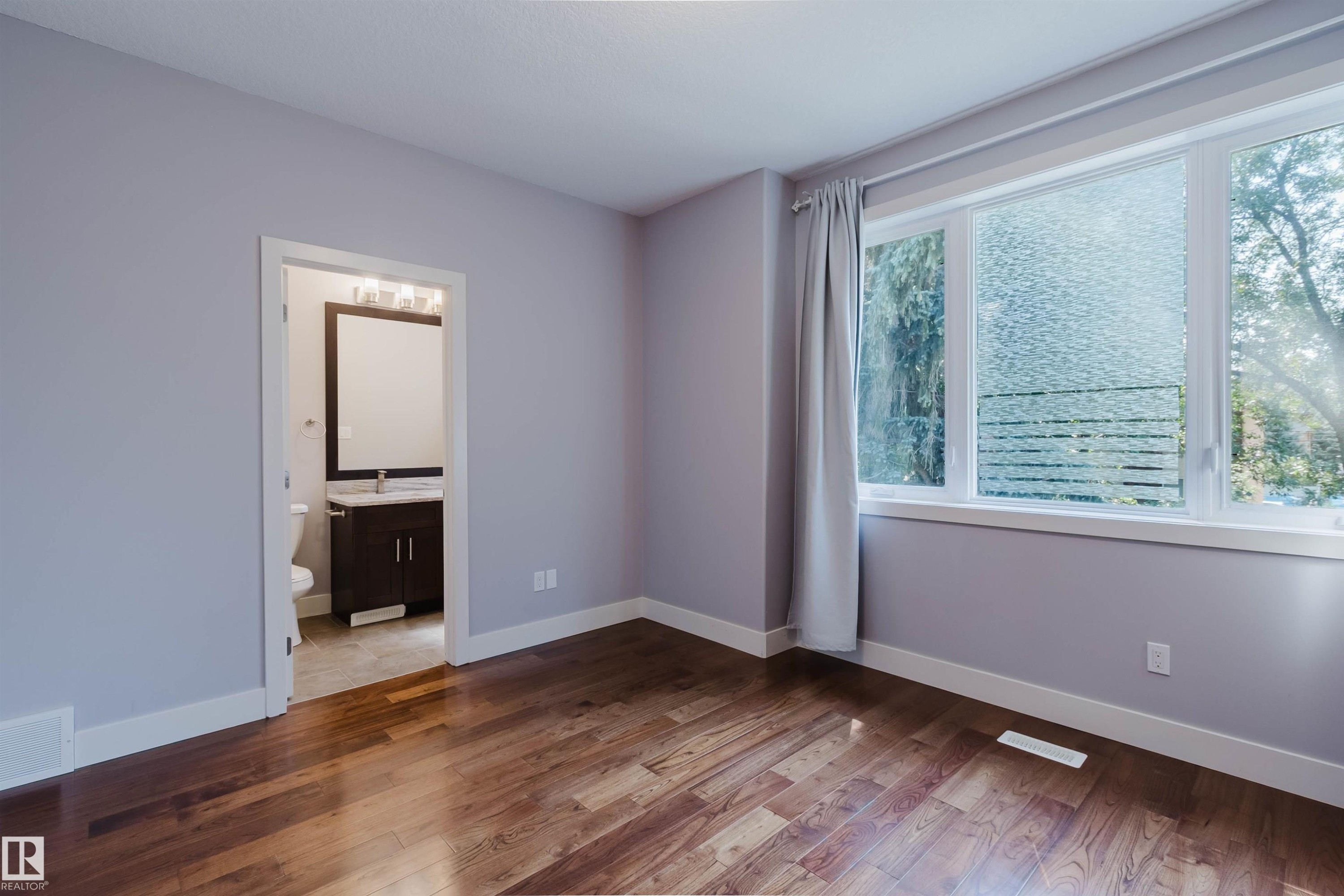 Spacious room featuring rich wood-finish flooring, light violet walls, and bright white trim - 10626 81 Avenue Nw, Edmonton, AB - Indoor Photo Showing Other Room