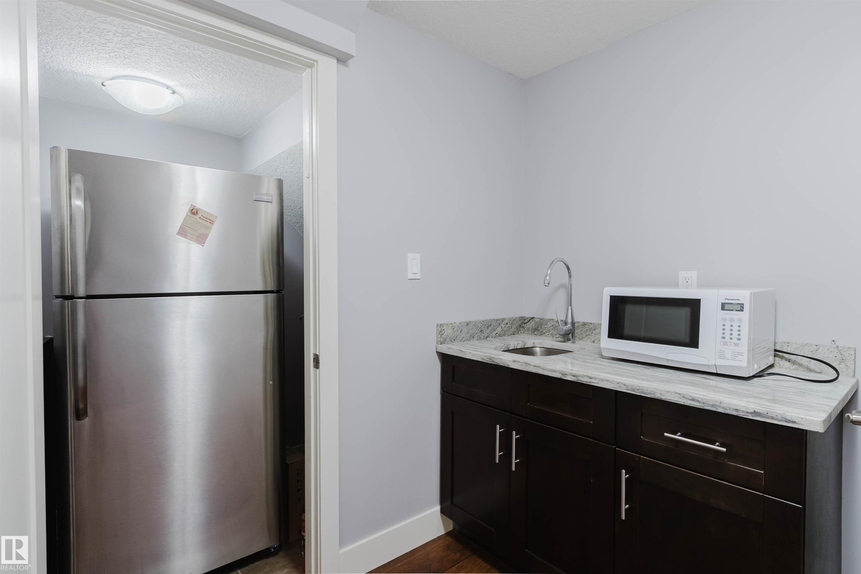 Compact kitchenette featuring dark wood-finish cabinetry, a stone countertop, and an undermount sink with a gooseneck faucet - 10626 81 Avenue Nw, Edmonton, AB - Indoor