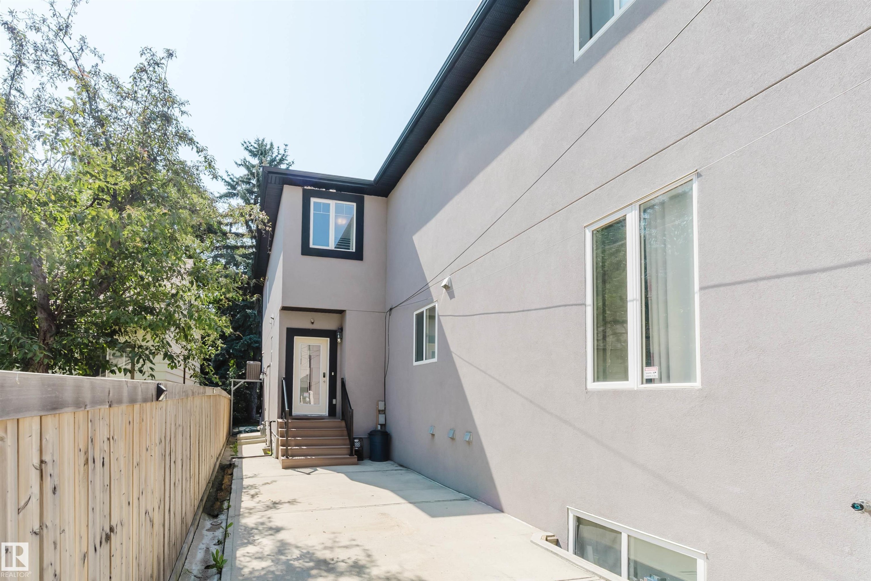 Contemporary stucco exterior with contrasting black trim, multiple white-framed windows, and a private wooden fence - 10626 81 Avenue Nw, Edmonton, AB - Outdoor With Exterior