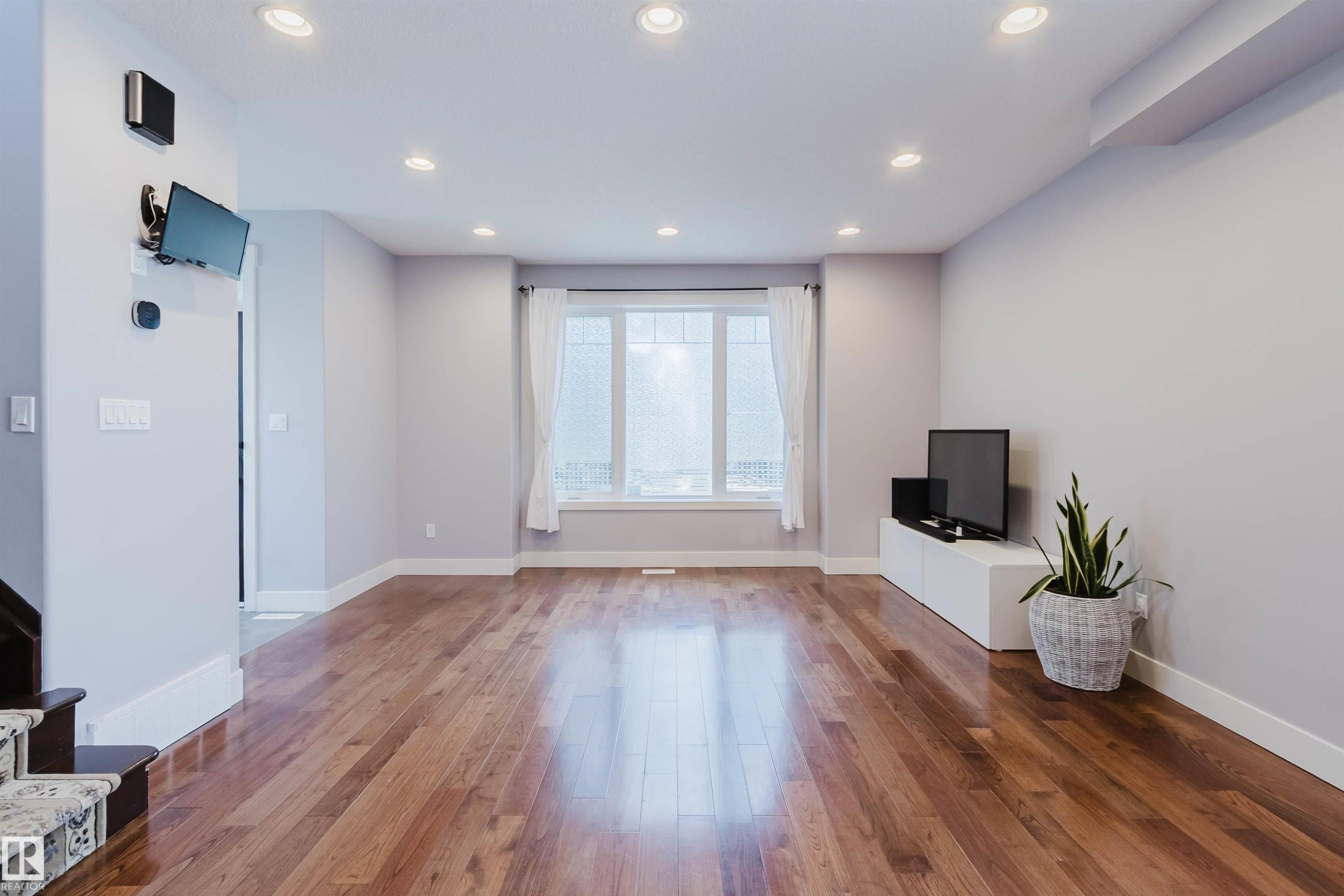 Expansive living space featuring rich wood-finish flooring, recessed ceiling lights, and crisp white baseboards - 10626 81 Avenue Nw, Edmonton, AB - Indoor Photo Showing Other Room