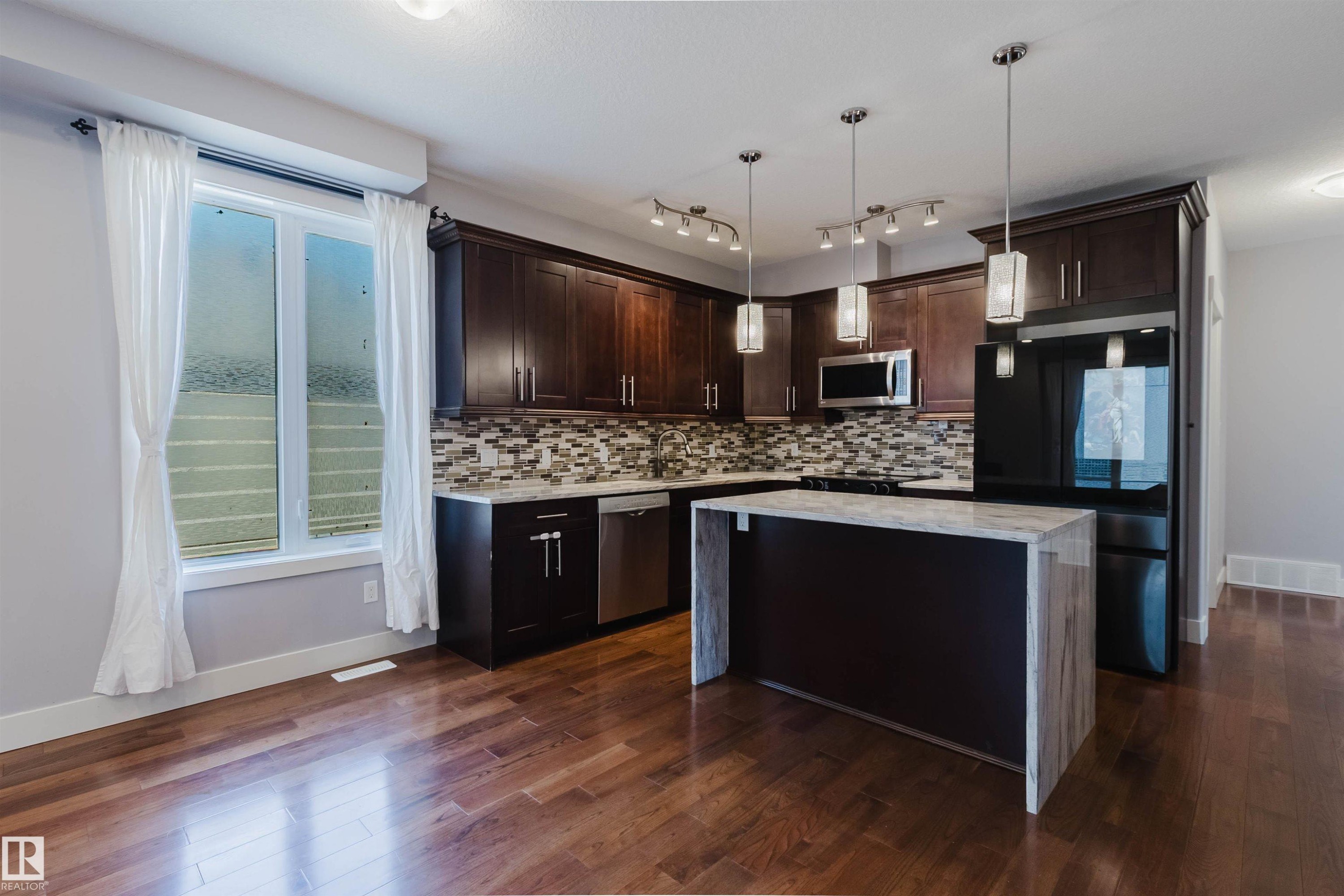Kitchen featuring rich wood cabinetry, stainless steel appliances, and a mosaic tile backsplash - 10626 81 Avenue Nw, Edmonton, AB - Indoor Photo Showing Kitchen With Upgraded Kitchen