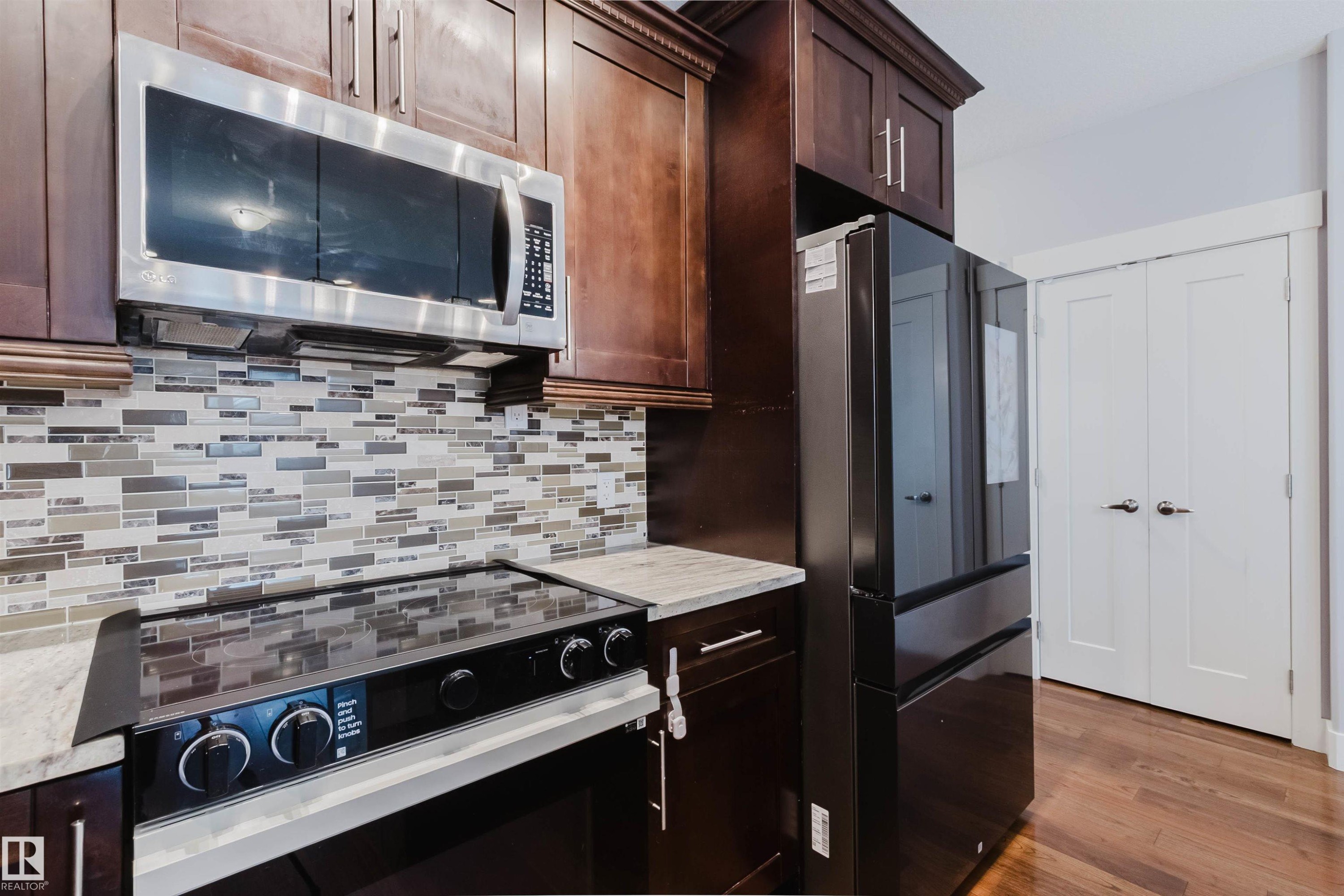 Kitchen featuring rich wood cabinetry, stainless steel appliances, a mosaic tile backsplash, and light-toned countertops - 10626 81 Avenue Nw, Edmonton, AB - Indoor Photo Showing Kitchen