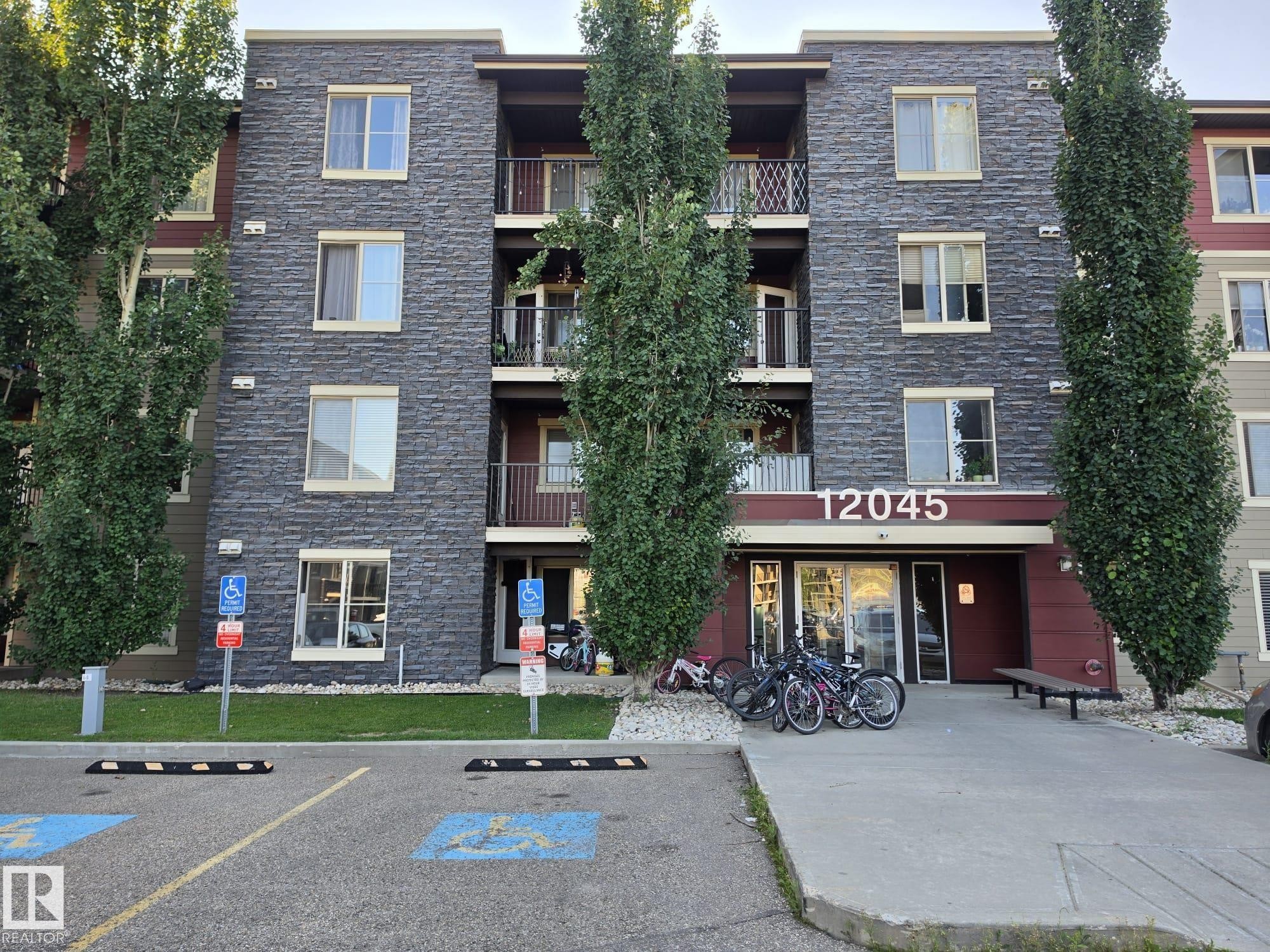 Multi-story building featuring a stone veneer facade, balconies with metal railings, and a prominent entrance with an overhead awning - #415 12045 22 Av Sw, Edmonton, AB - Outdoor With Balcony With Facade