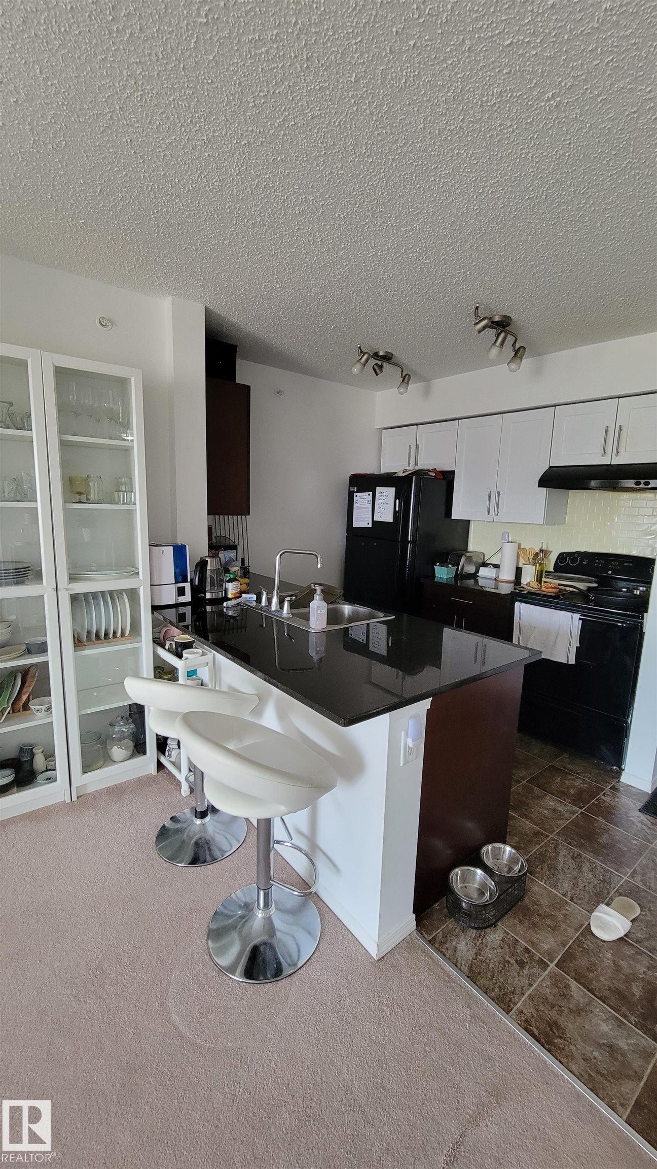 Kitchen featuring white upper cabinetry, dark lower cabinetry, and a dark countertop island with an integrated sink - #415 12045 22 Av Sw, Edmonton, AB - Indoor