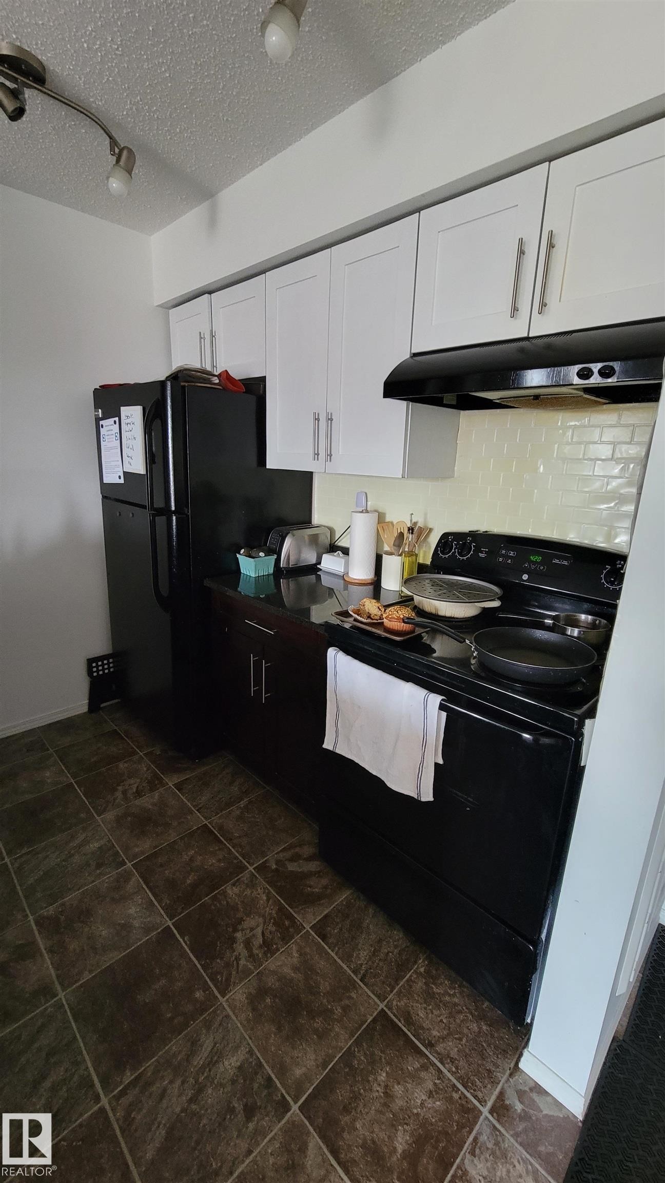 Kitchen featuring white upper cabinetry, dark lower cabinetry, and black appliances - #415 12045 22 Av Sw, Edmonton, AB - Indoor Photo Showing Kitchen