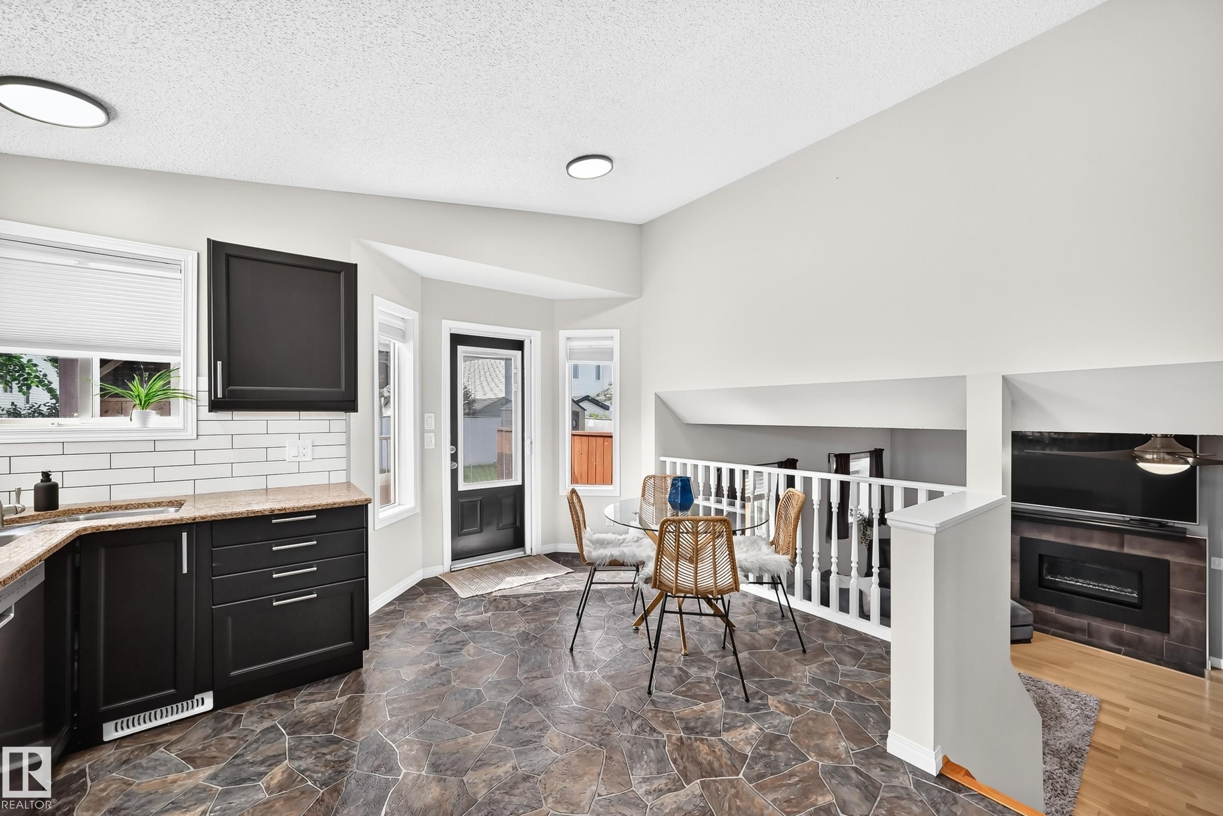 Kitchen and dining area featuring dark cabinetry, light granite-finish countertops, subway tile backsplash, and irregular-cut stone-finish flooring - 3729 131A Avenue Nw, Edmonton, AB - Indoor