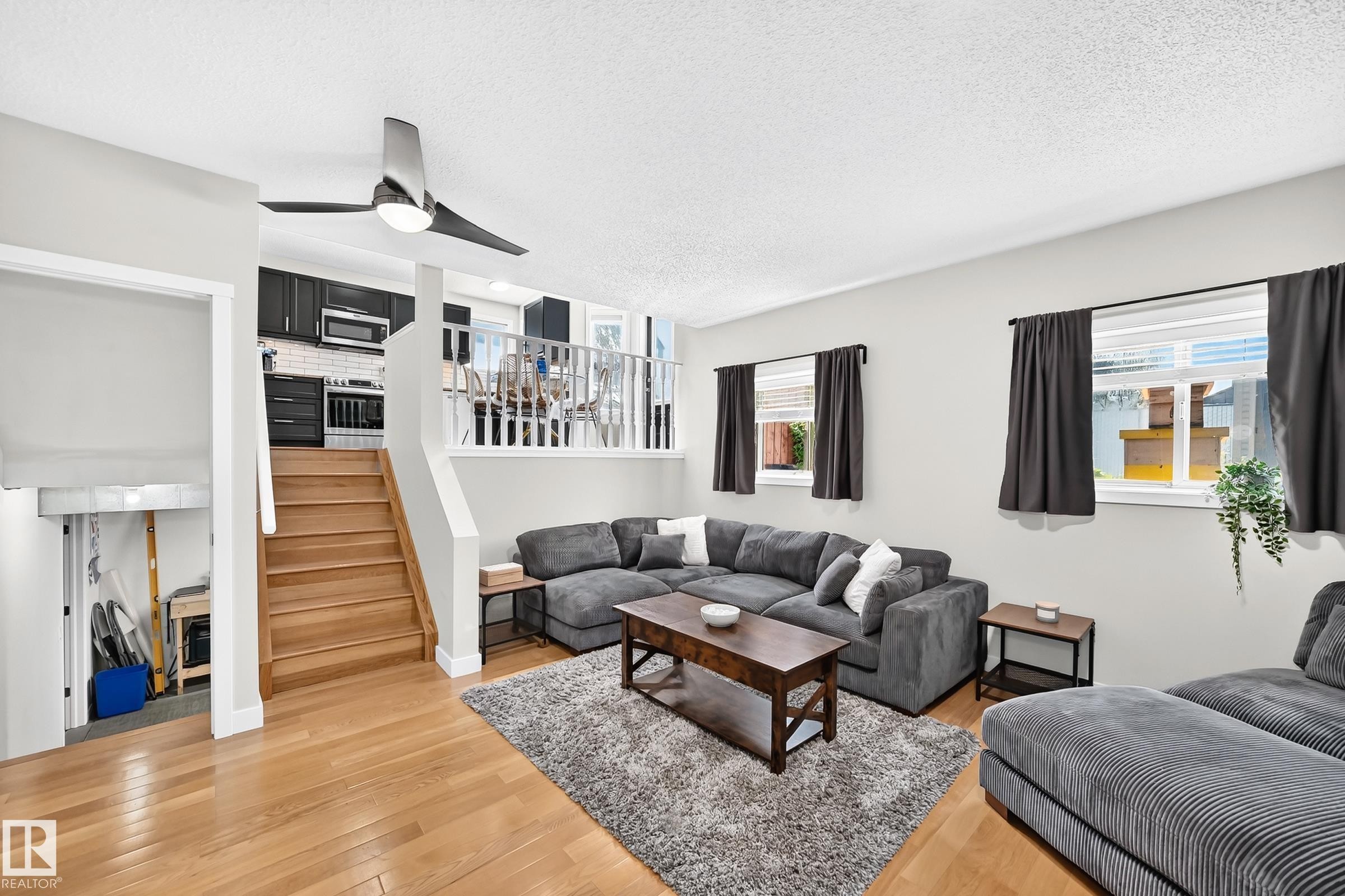 Open-concept living area featuring wood-finish flooring, a modern ceiling fan, and multiple windows with blinds - 3729 131A Avenue Nw, Edmonton, AB - Indoor Photo Showing Living Room