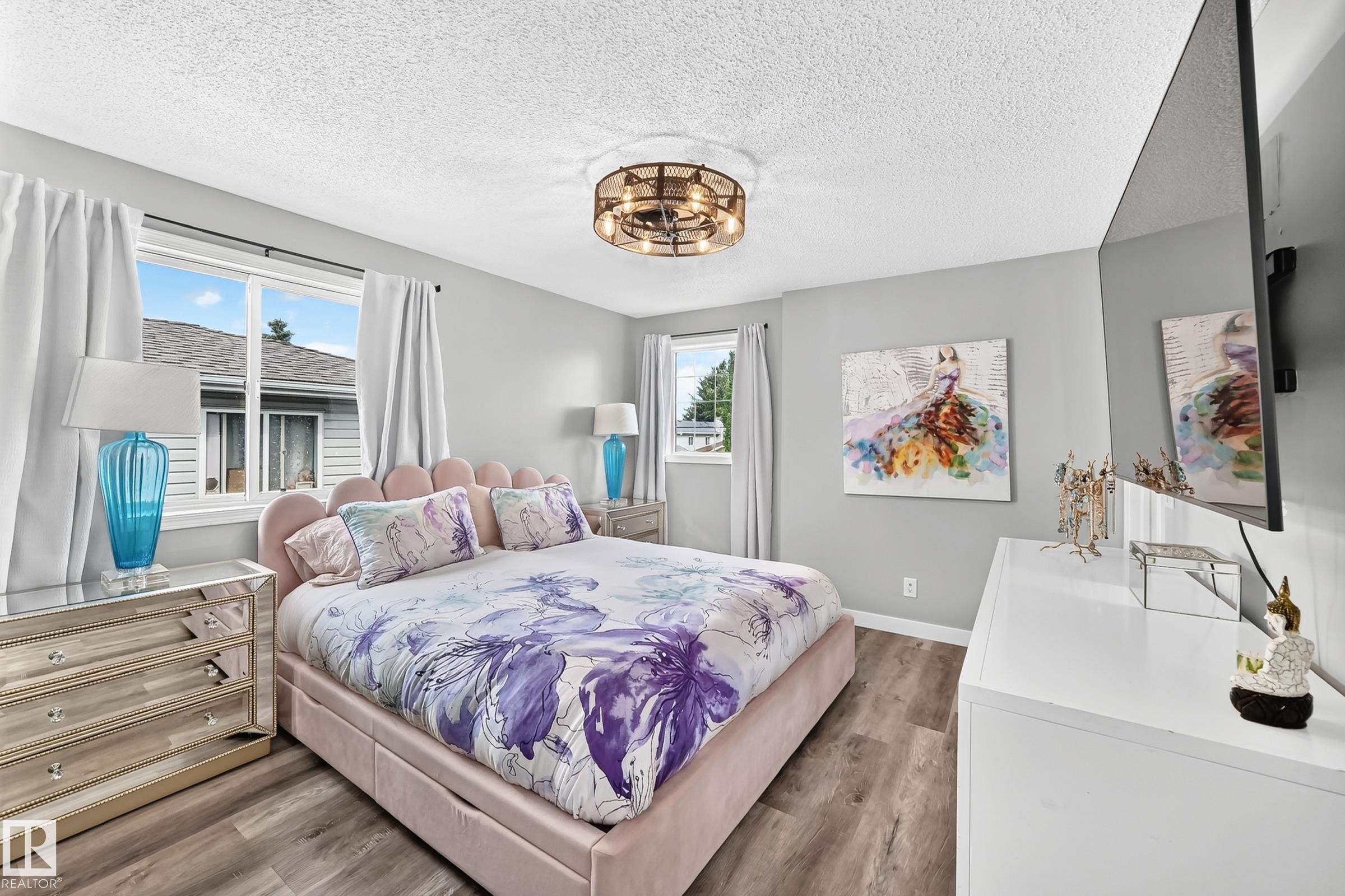 Light-filled bedroom featuring wood-finish flooring, two large windows with white curtains, a textured ceiling, and a circular overhead light fixture - 3729 131A Avenue Nw, Edmonton, AB - Indoor Photo Showing Bedroom