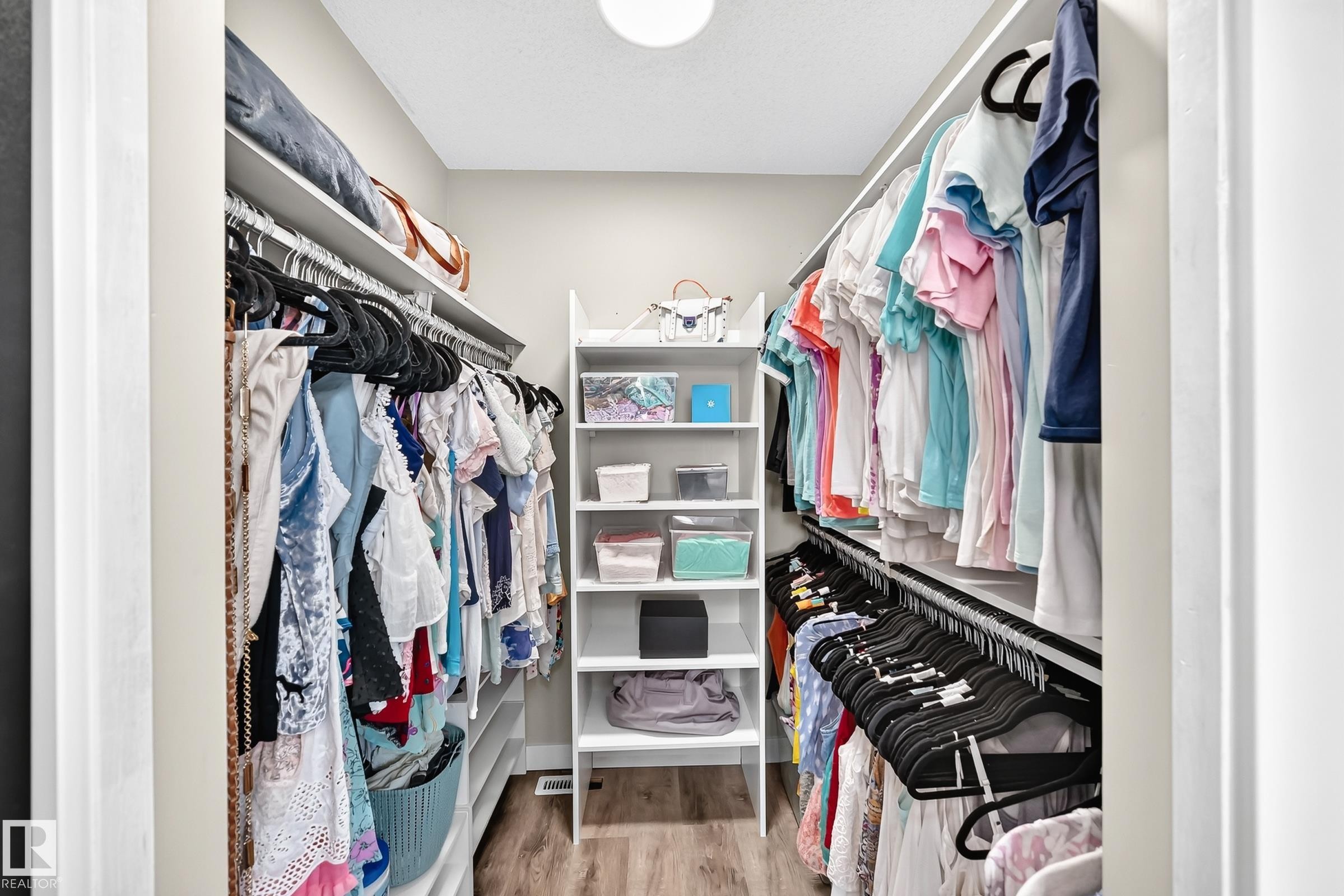 Walk-in closet featuring built-in shelving, dual hanging rods, a central storage unit with open shelving, and wood-finish flooring - 3729 131A Avenue Nw, Edmonton, AB - Indoor With Storage