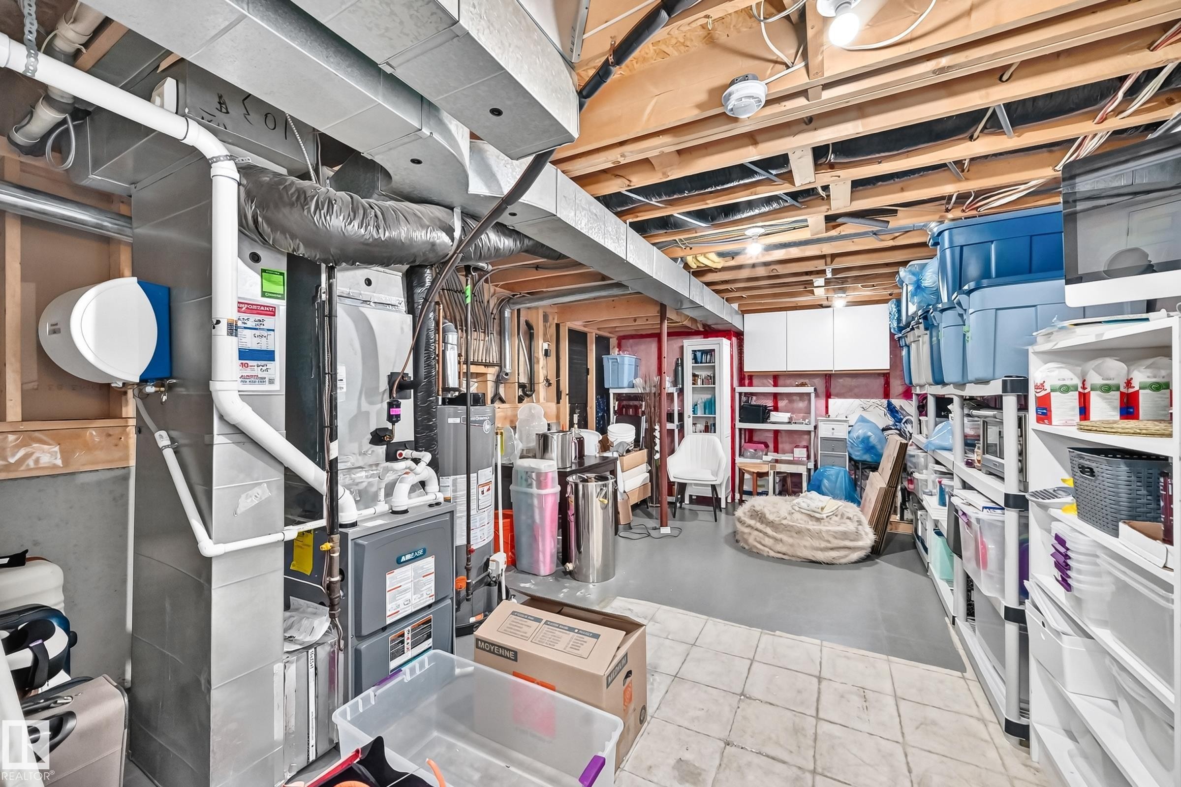 Utility area featuring exposed ceiling joists and ductwork, a water heater, a furnace, and white wall cabinetry - 3729 131A Avenue Nw, Edmonton, AB - Indoor Photo Showing Basement