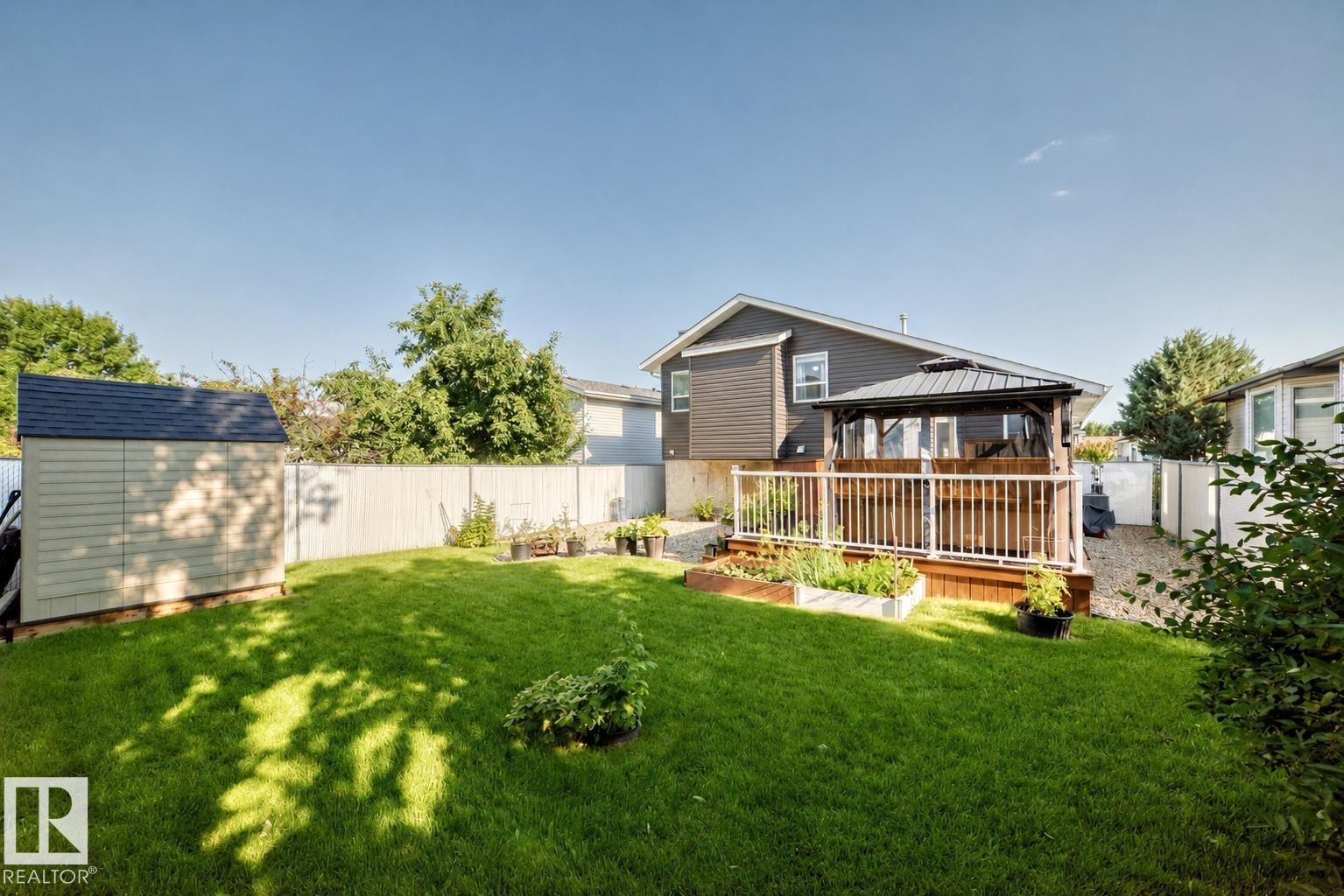 Expansive backyard featuring a manicured lawn, a detached storage shed with a shingled roof, a spacious wood-finish deck with white railings, and a built-in gazebo with a dark roof - 3729 131A Avenue Nw, Edmonton, AB - Outdoor With Deck Patio Veranda