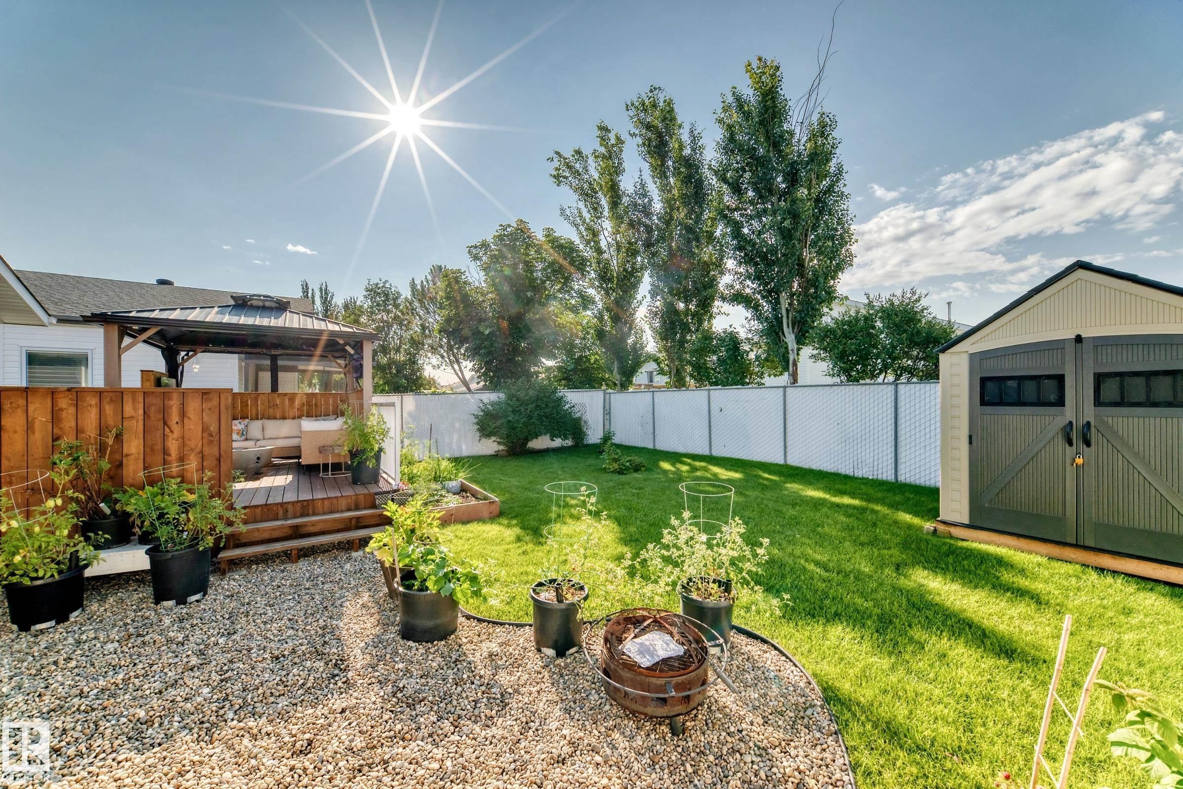 Expansive backyard with a manicured lawn, a raised wooden deck with a gazebo, a gravel patio area, a raised garden bed, and a detached storage shed - 3729 131A Avenue Nw, Edmonton, AB - Outdoor With Deck Patio Veranda