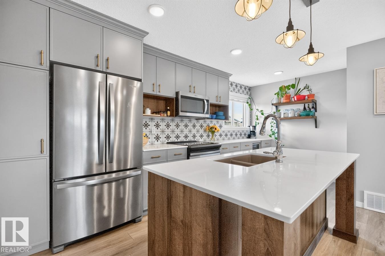 Open Concept Kitchen featuring Stainless Steel Appliances, Stylish Lighting and Accent Tiles, Bar Fridge, and Bar/Counter Seating. - 1051 Cy Becker Road Nw, Edmonton, AB - Indoor Photo Showing Kitchen With Double Sink With Upgraded Kitchen