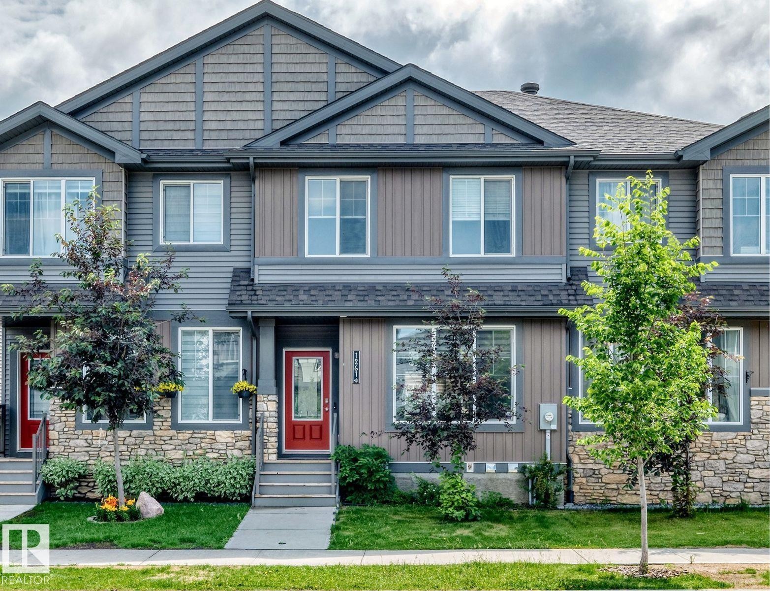Townhouse exterior featuring a red entry door, gray siding, stone accents, and a gabled roofline - 1261 Rosenthal Boulevard Nw, Edmonton, AB - Outdoor With Facade