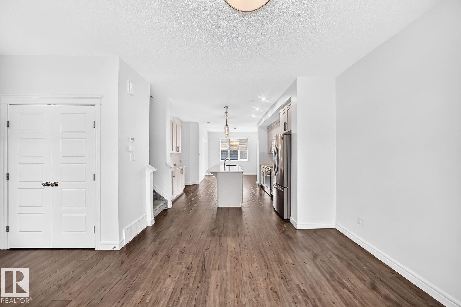 Open-concept living area featuring wood-finish flooring, white walls, and a recessed kitchen with stainless steel appliances - 1261 Rosenthal Boulevard Nw, Edmonton, AB - Indoor