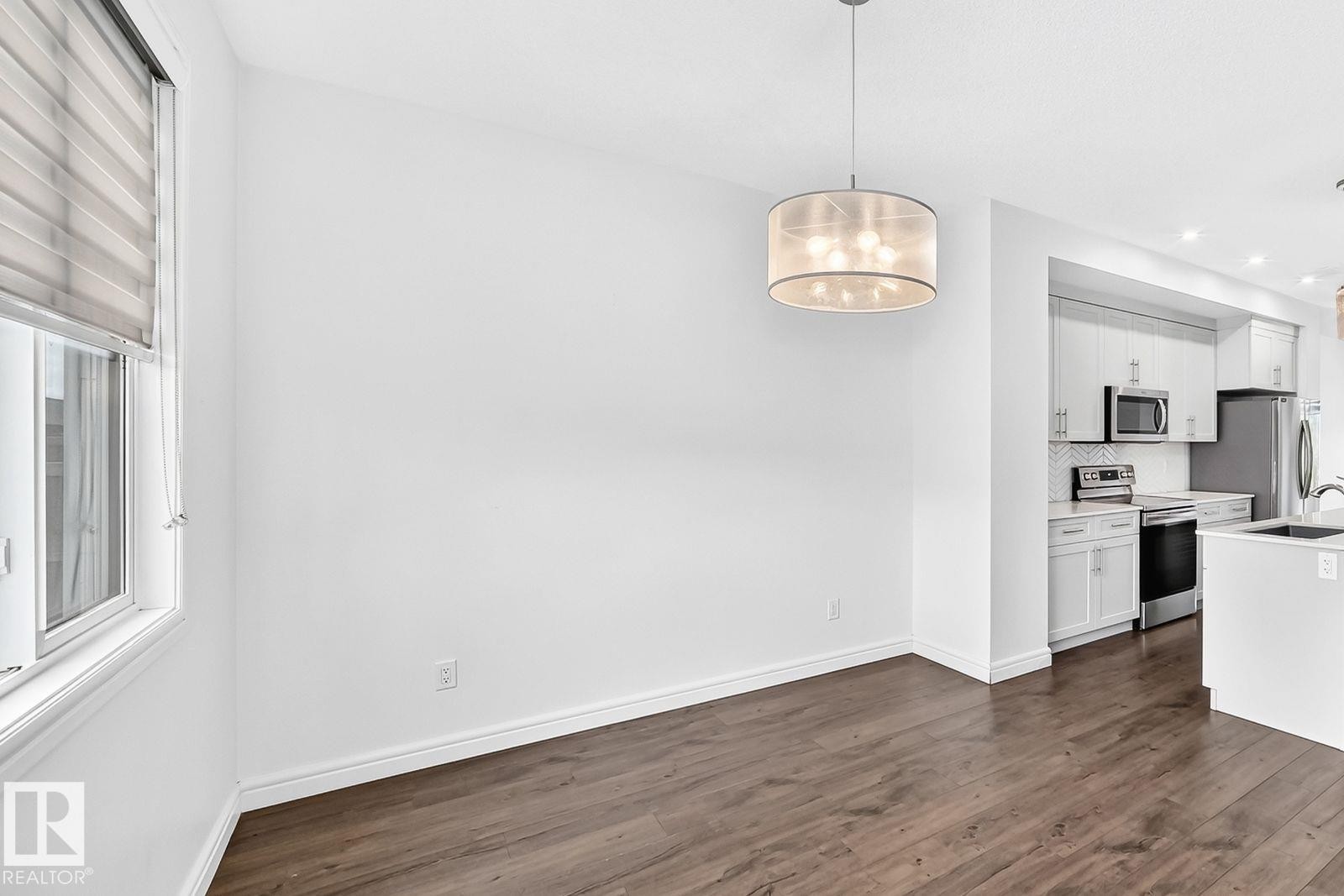 Open-concept dining area with wood-finish flooring, a contemporary drum pendant light, and a window with blinds - 1261 Rosenthal Boulevard Nw, Edmonton, AB - Indoor Photo Showing Kitchen