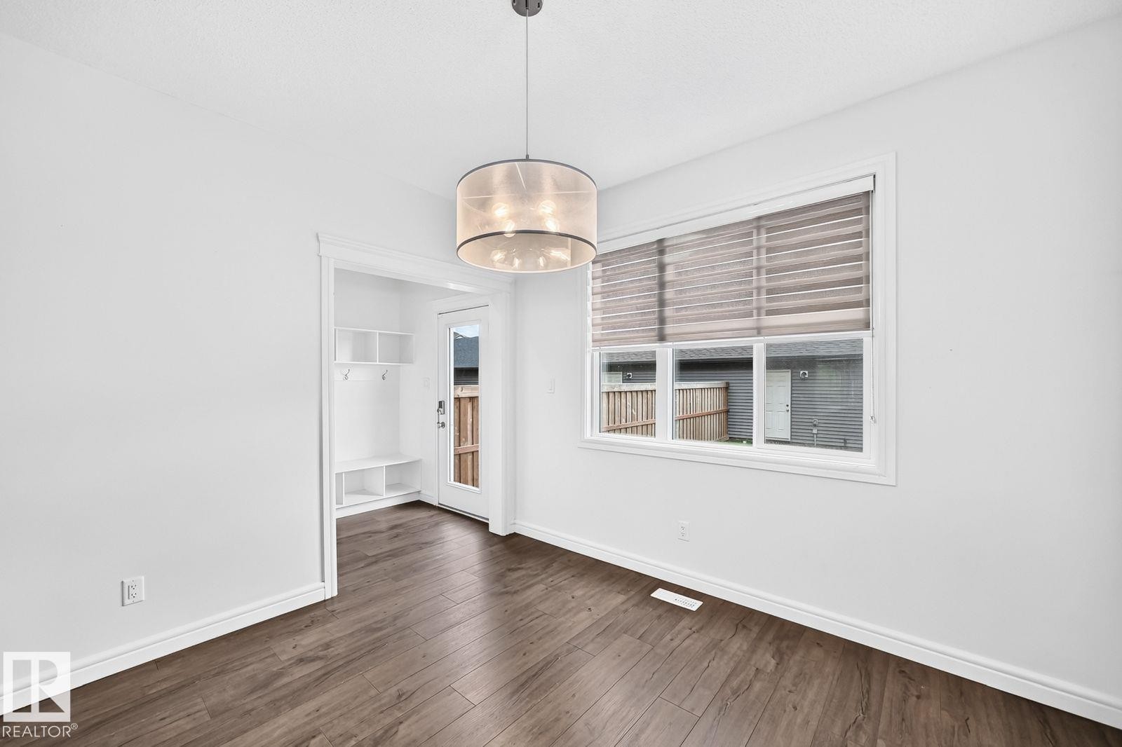 Bright interior space featuring wood-finish flooring, a contemporary drum pendant light fixture, and white trim - 1261 Rosenthal Boulevard Nw, Edmonton, AB - Indoor Photo Showing Other Room