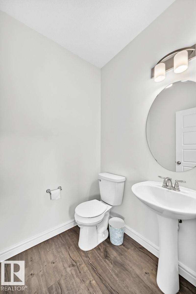 Powder room featuring a pedestal sink with a chrome faucet, a circular mirror, and a three-light vanity fixture - 1261 Rosenthal Boulevard Nw, Edmonton, AB - Indoor Photo Showing Bathroom
