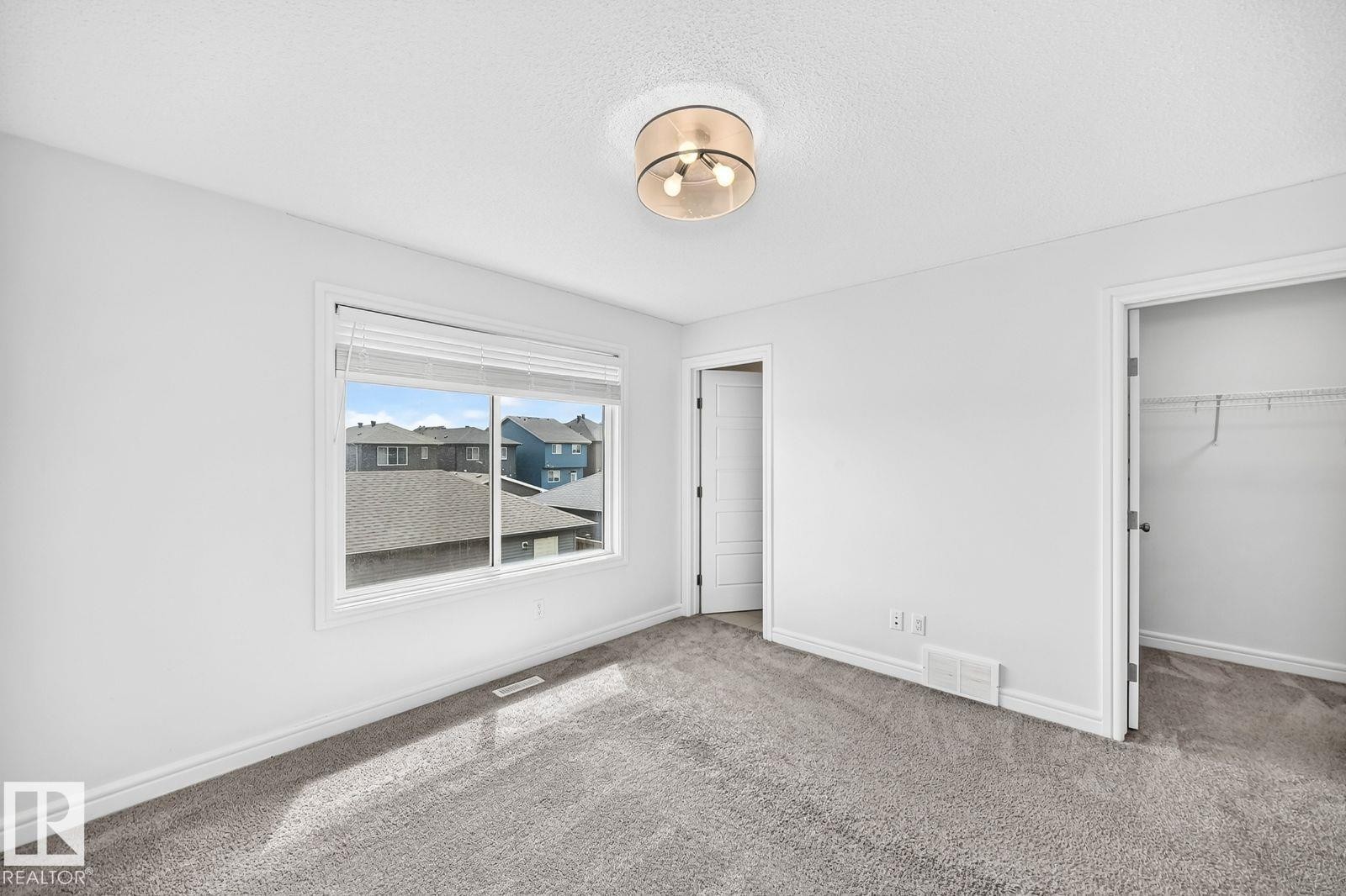 Carpeted room featuring a large window, a ceiling-mounted light fixture, a paneled door, and a closet with wire shelving - 1261 Rosenthal Boulevard Nw, Edmonton, AB - Indoor Photo Showing Other Room