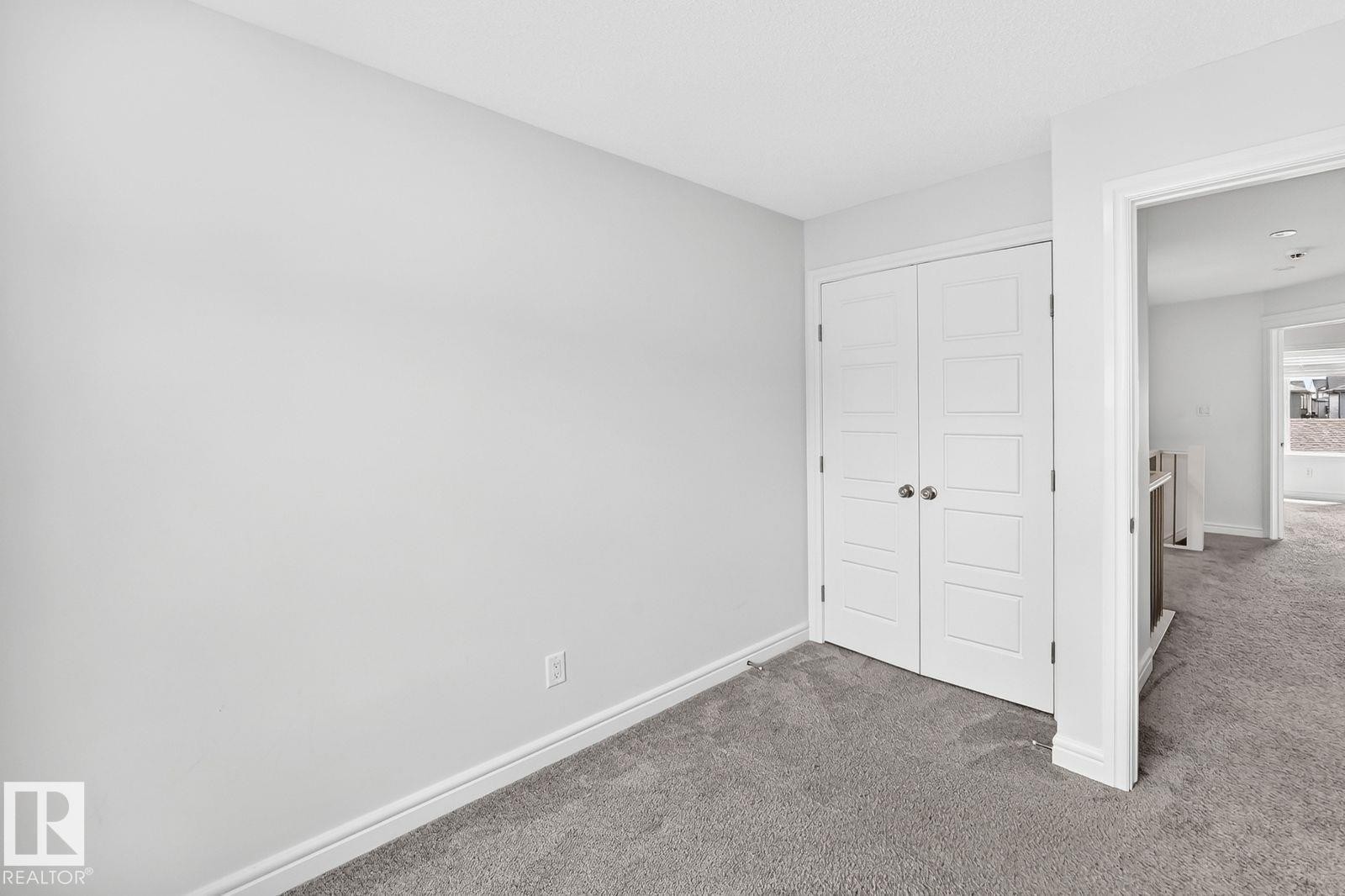 Carpeted room featuring a white paneled bi-fold closet door with satin nickel hardware, light gray walls, and white baseboards - 1261 Rosenthal Boulevard Nw, Edmonton, AB - Indoor Photo Showing Other Room