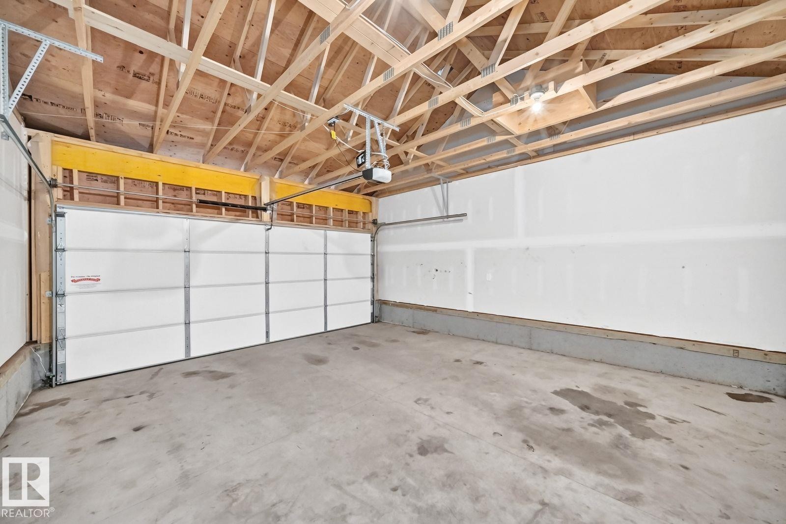 Spacious garage featuring a concrete floor, a white paneled garage door with an automatic opener, exposed ceiling trusses, and white drywall walls - 1261 Rosenthal Boulevard Nw, Edmonton, AB - Indoor Photo Showing Garage