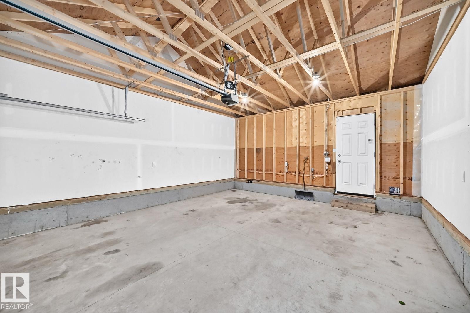 Spacious garage featuring a concrete floor, exposed wooden rafters, and an automatic garage door opener - 1261 Rosenthal Boulevard Nw, Edmonton, AB - Indoor Photo Showing Garage