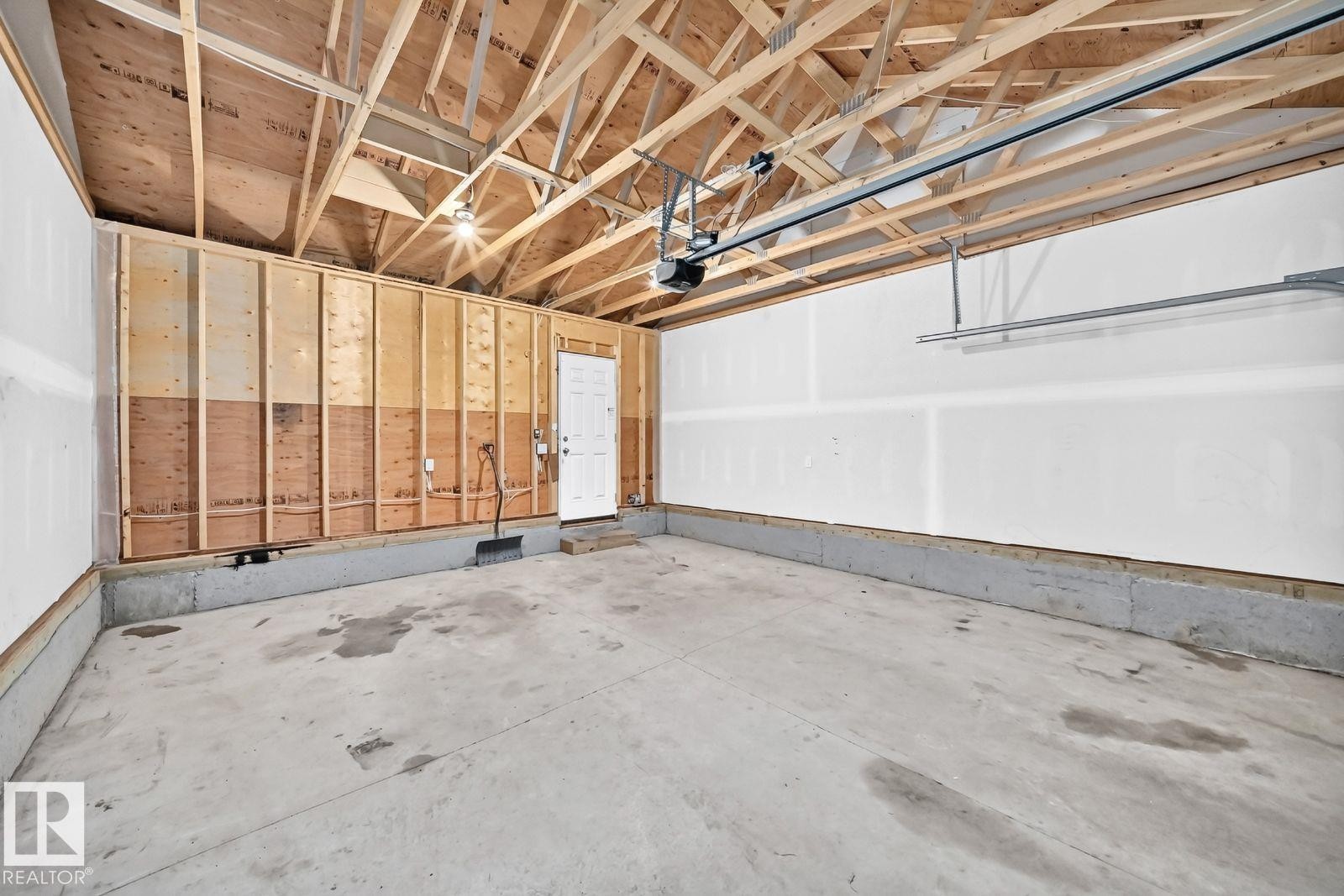 Spacious garage featuring a concrete floor, exposed wooden ceiling trusses, and an automatic garage door opener - 1261 Rosenthal Boulevard Nw, Edmonton, AB - Indoor Photo Showing Garage