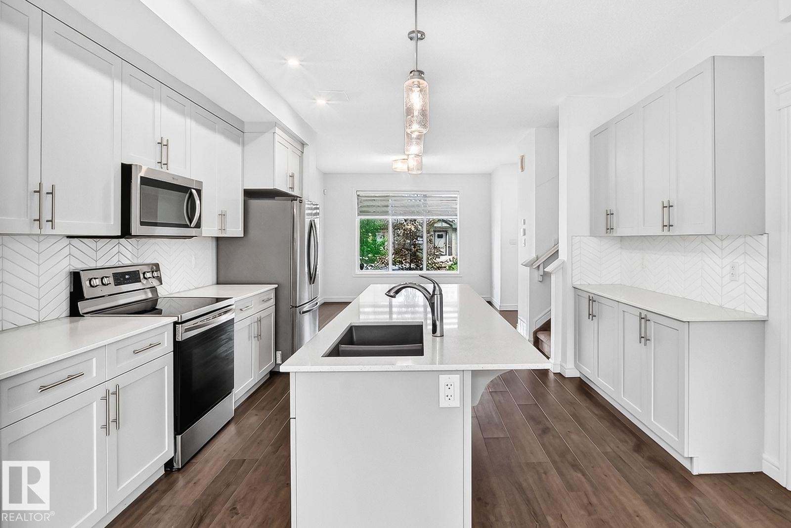 Modern kitchen featuring a central island with an undermount sink, pendant lighting, stainless steel appliances, white cabinetry, and wood-finish flooring - 1261 Rosenthal Boulevard Nw, Edmonton, AB - Indoor Photo Showing Kitchen With Double Sink With Upgraded Kitchen