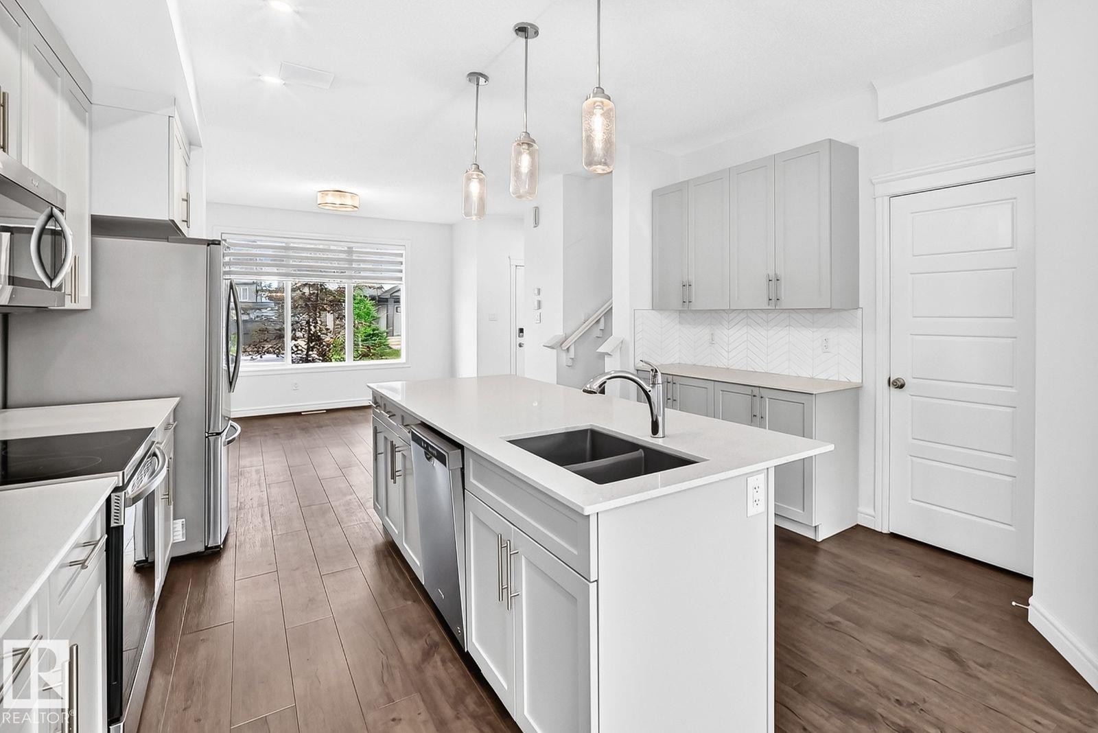 Open-concept kitchen featuring an island with an undermount sink, stainless steel appliances, light gray cabinetry, and wood-finish flooring - 1261 Rosenthal Boulevard Nw, Edmonton, AB - Indoor Photo Showing Kitchen With Double Sink With Upgraded Kitchen