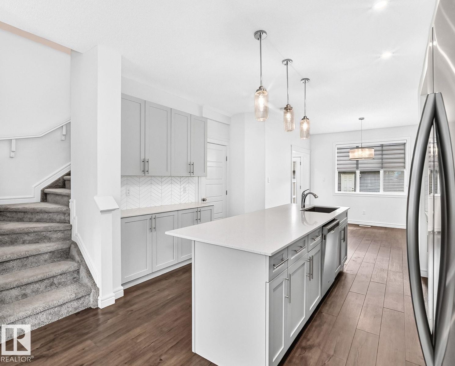 Modern kitchen featuring an island with a built-in sink, stainless steel appliances, light gray cabinetry, and a white herringbone tile backsplash - 1261 Rosenthal Boulevard Nw, Edmonton, AB - Indoor Photo Showing Kitchen With Upgraded Kitchen