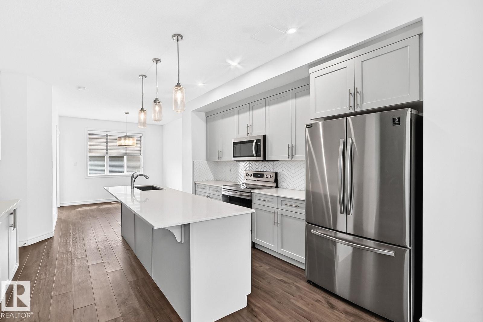 Contemporary kitchen featuring light gray cabinetry, stainless steel appliances, a white herringbone tile backsplash, and a spacious kitchen island with an undermount sink - 1261 Rosenthal Boulevard Nw, Edmonton, AB - Indoor Photo Showing Kitchen With Upgraded Kitchen