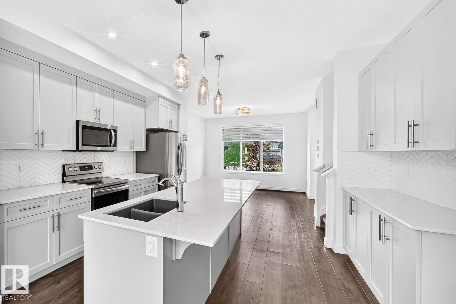 Open-concept kitchen featuring an oversized island with a dual-basin sink, quartz countertops, stainless steel appliances, and a chevron tile backsplash - 1261 Rosenthal Boulevard Nw, Edmonton, AB - Indoor Photo Showing Kitchen With Double Sink With Upgraded Kitchen