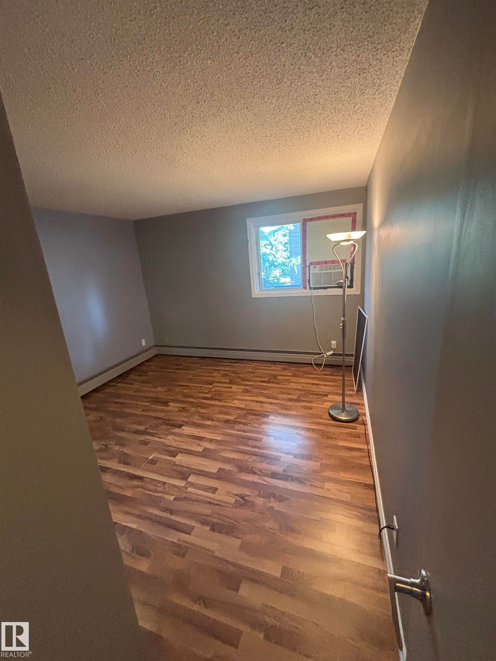 Spacious room featuring wood-finish flooring, a window with exterior views, and neutral wall paint - #206 2311 119 St Nw, Edmonton, AB - Indoor Photo Showing Other Room
