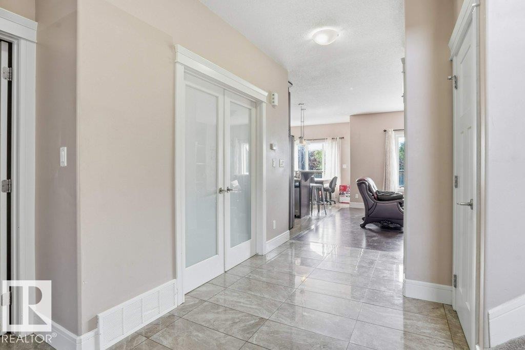 Foyer featuring large format tile flooring, frosted glass French doors, and substantial white baseboards - 258 Albany Drive Nw, Edmonton, AB - Indoor Photo Showing Other Room